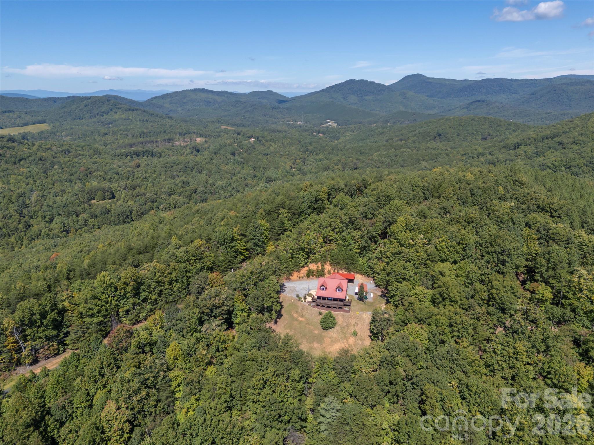 A red-roofed house sits in a forest clearing, surrounded by wooded mountain ridges.