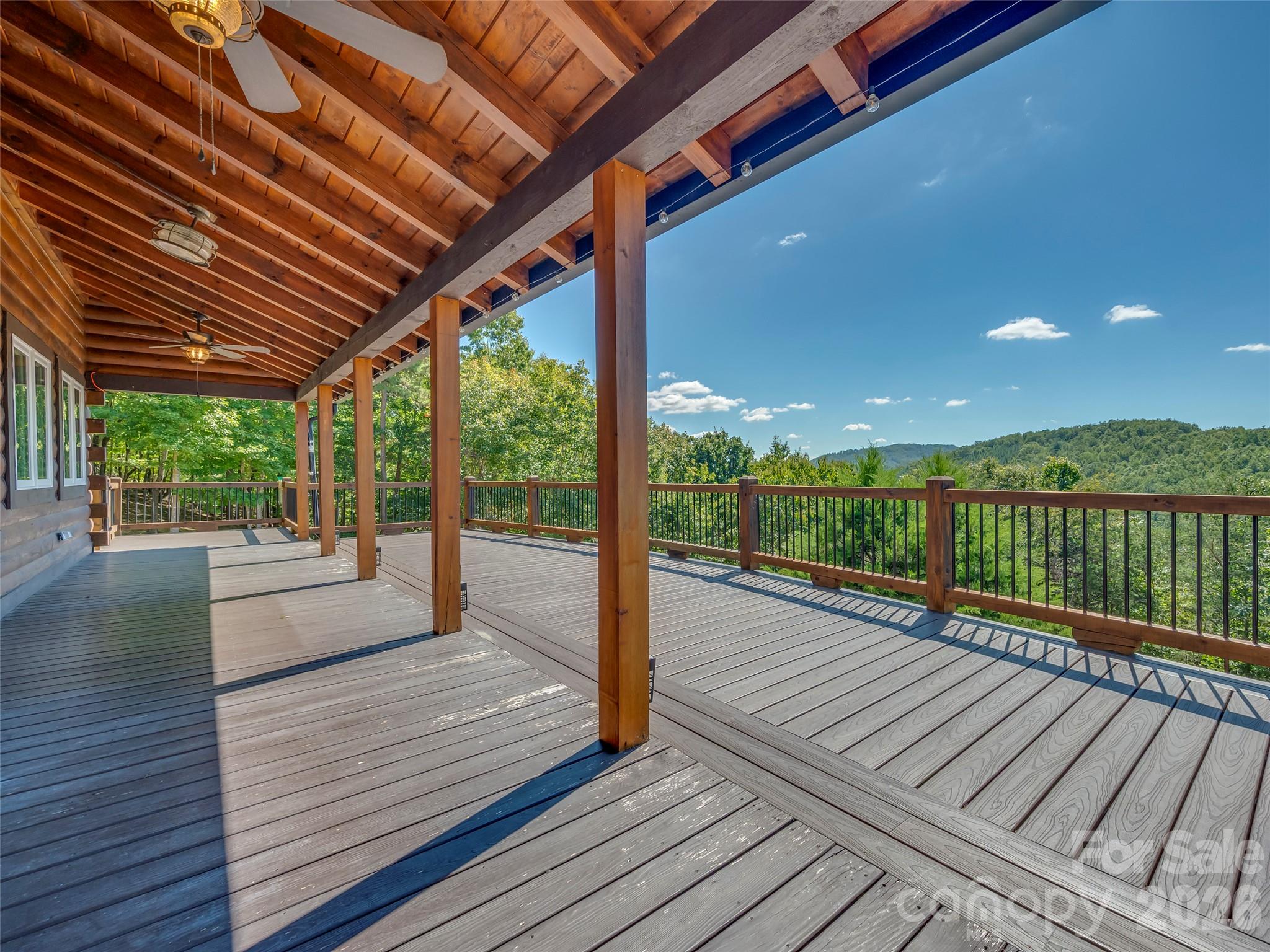 Covered wooden deck with ceiling fans and a view of forested hills.