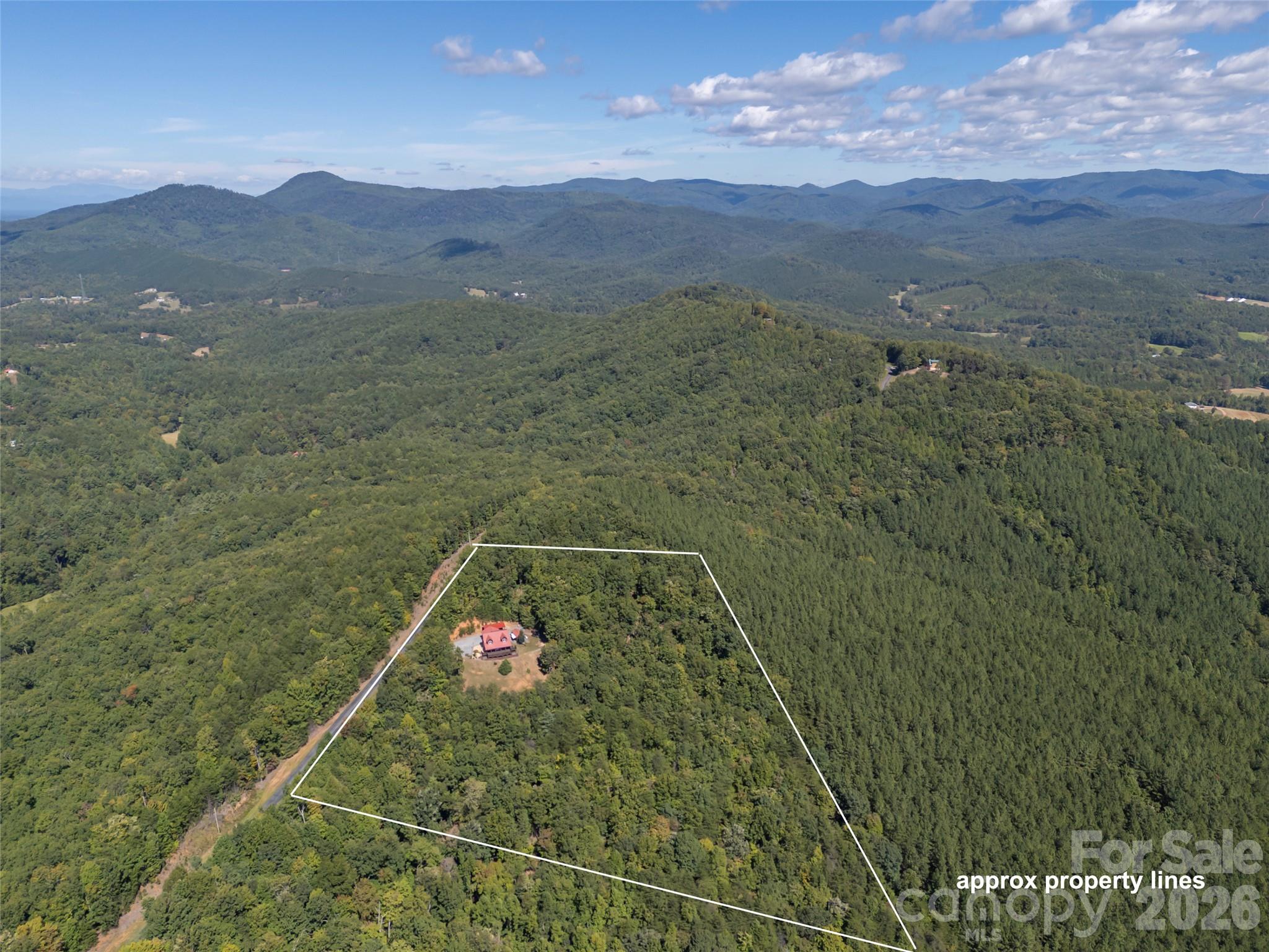 Aerial view of a wooded mountain parcel outlined in white, with a small red-roofed home and distant ridges.