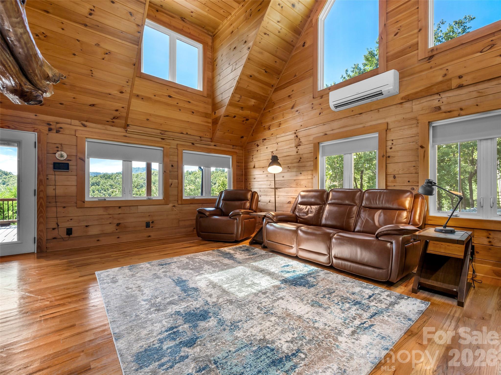 Cabin living room with vaulted wood ceiling, leather recliners, and windows overlooking wooded hills.