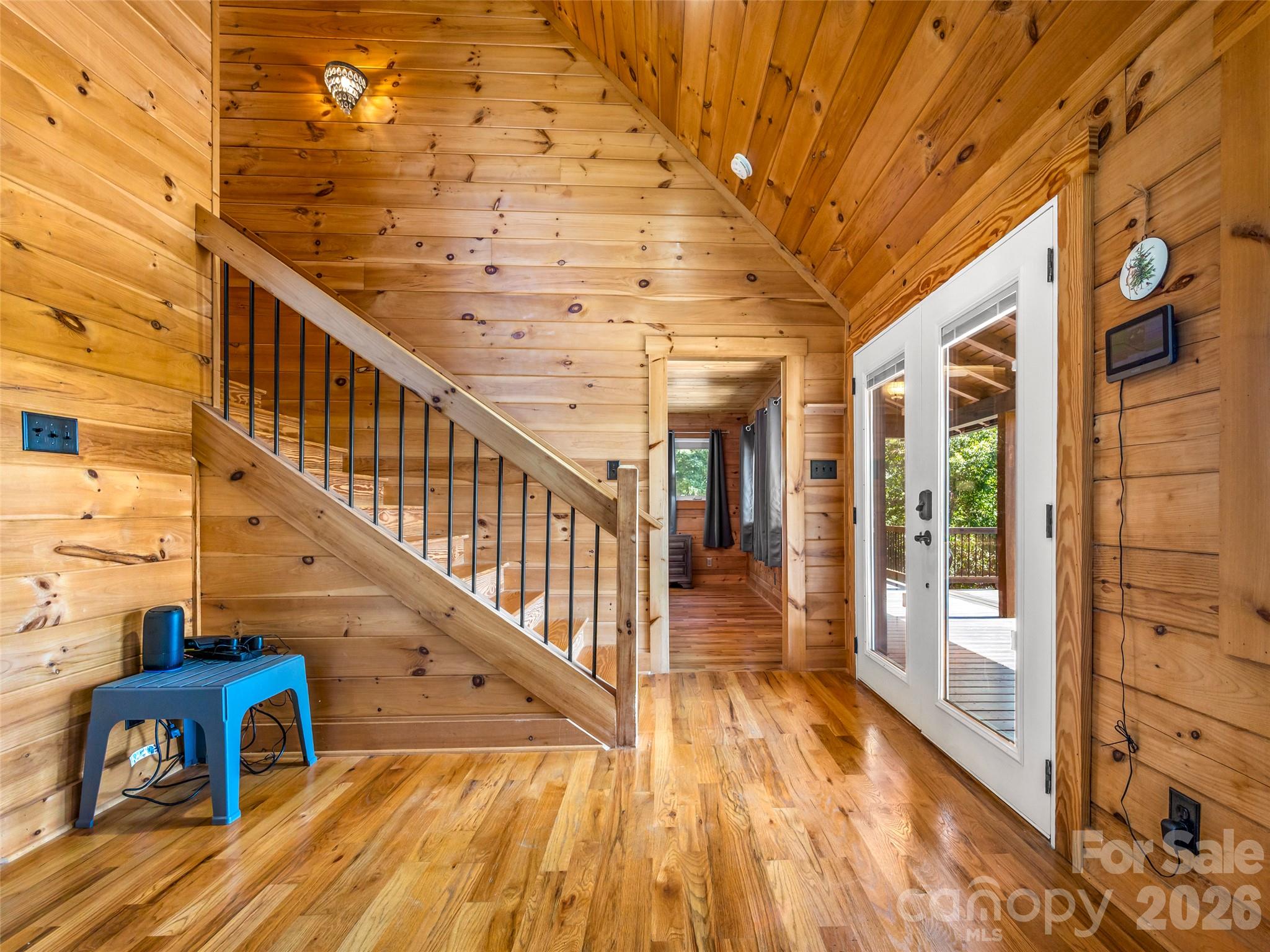 Cabin entryway with a wood staircase, hardwood floors, and glass doors opening onto a deck.