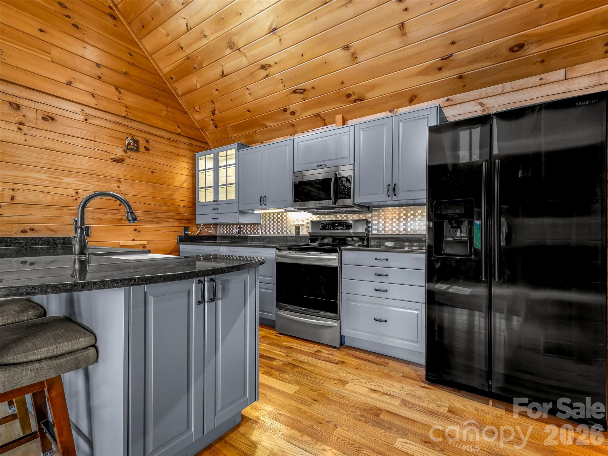Kitchen with gray cabinetry, black appliances, a stone island, and warm wood walls and ceiling.