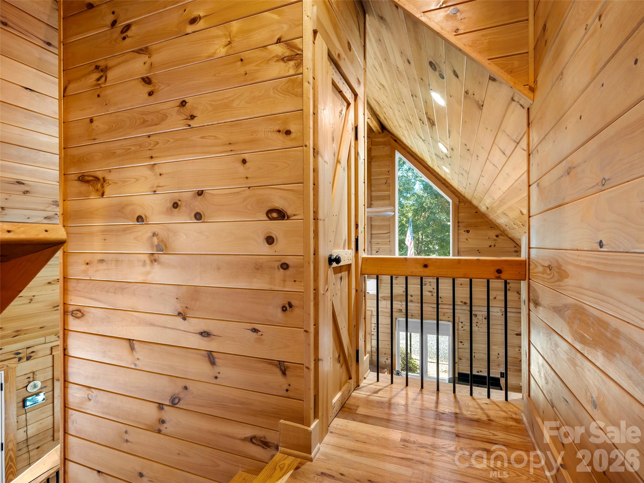 Wood-paneled stair landing with a vaulted ceiling and tall triangular window.