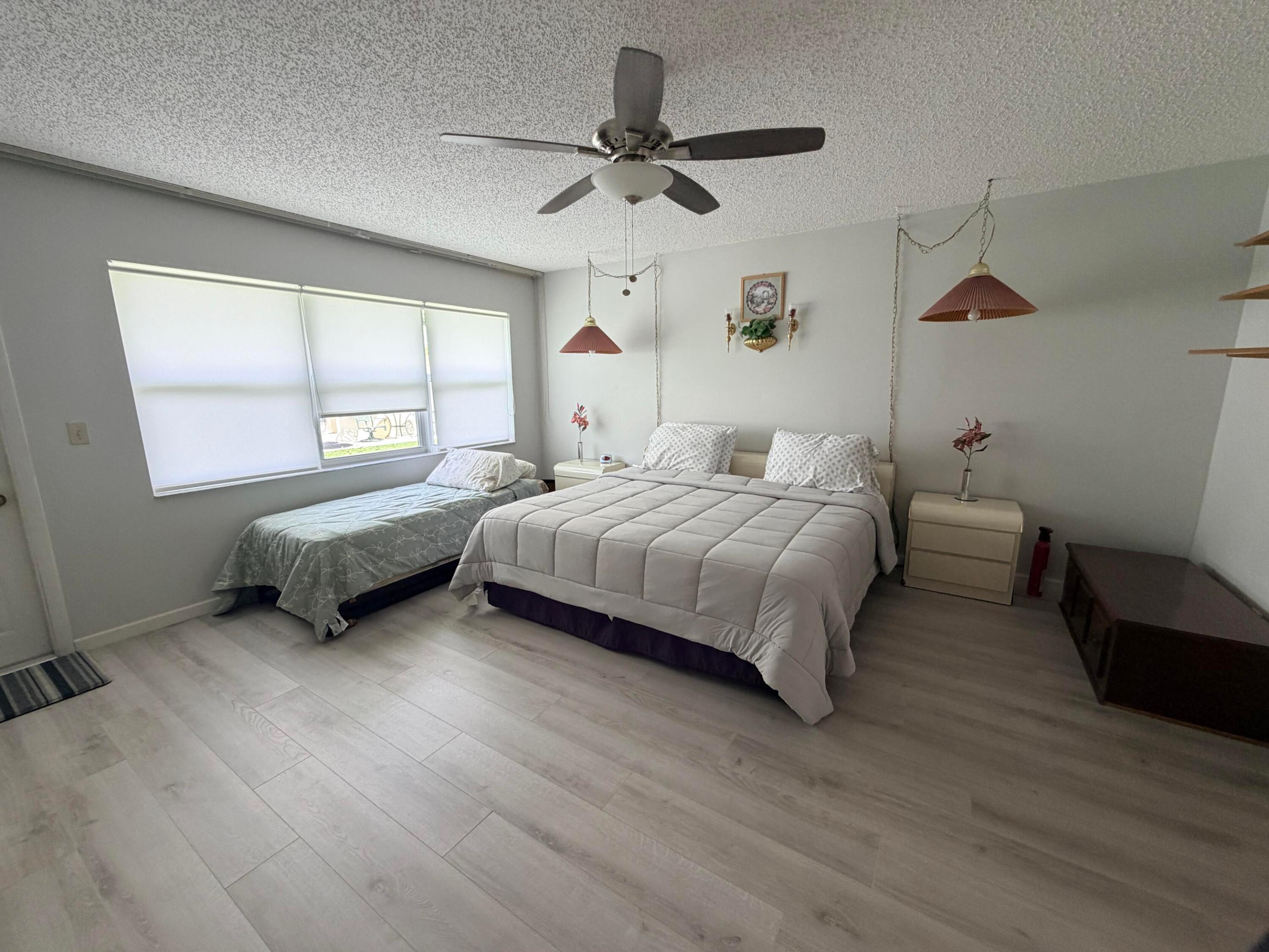 Bedroom with a large bed, twin bed, wide shaded window, and ceiling fan.