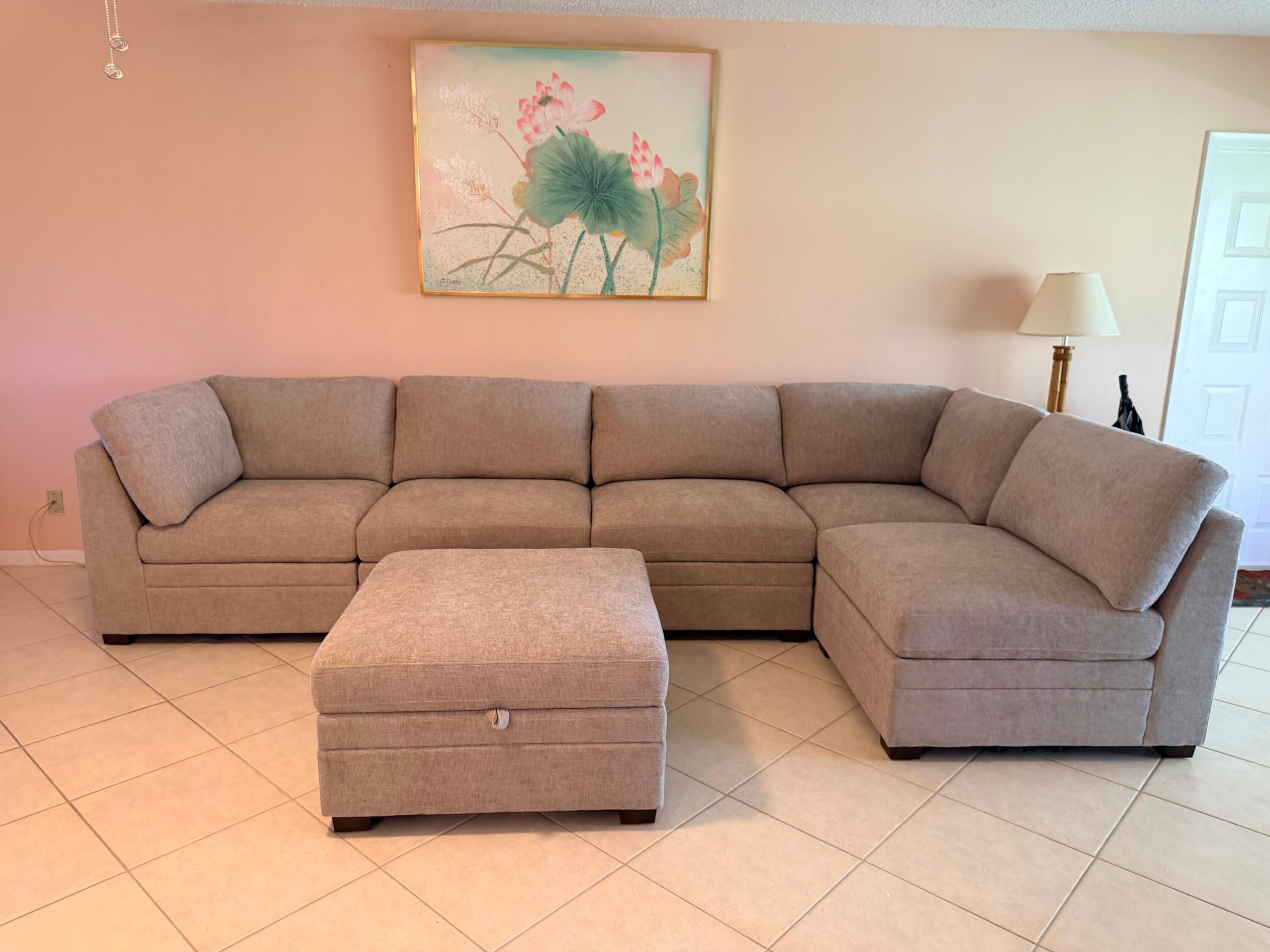 Living room with a taupe sectional and ottoman beneath a floral painting.