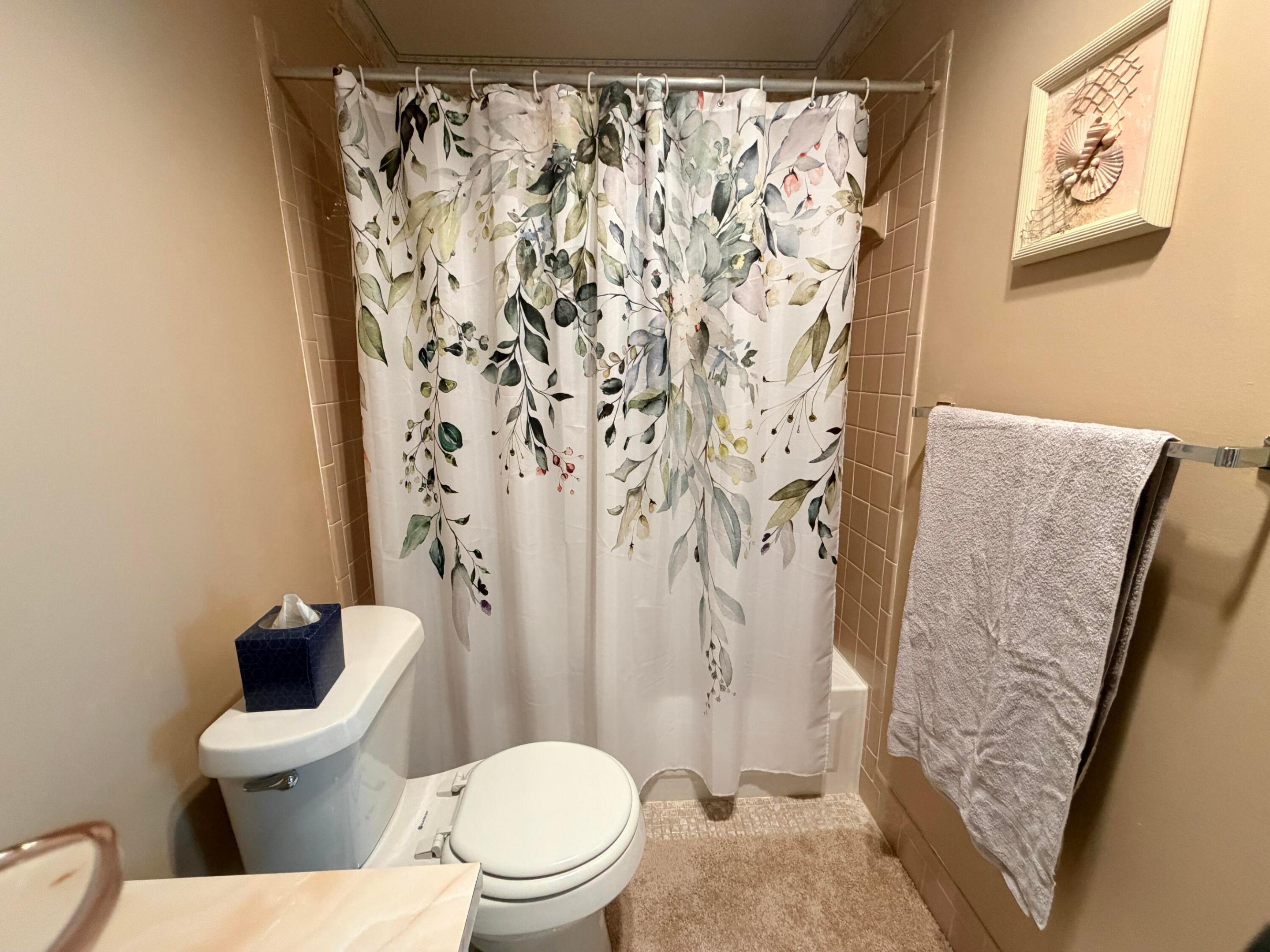 Bathroom with a botanical-print shower curtain, beige tile, white toilet, and towel rack.