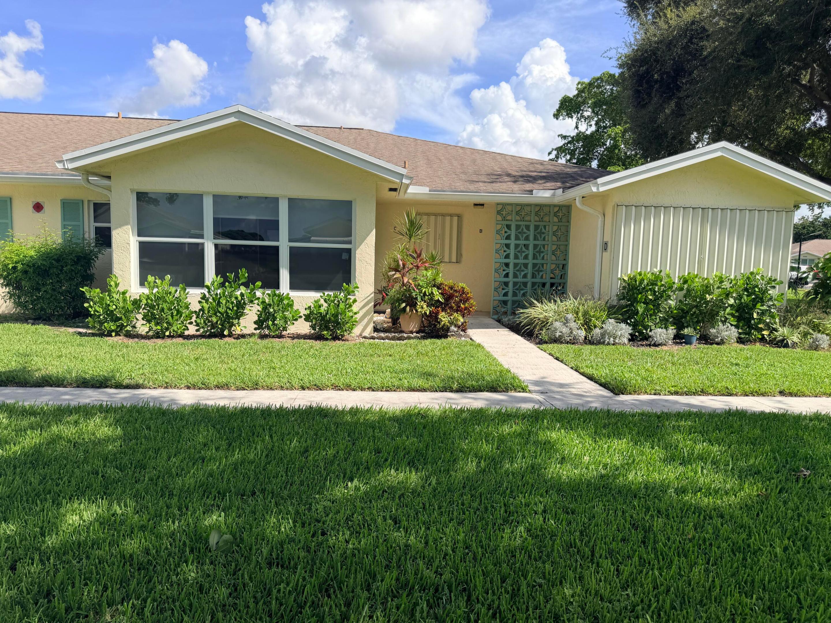 Single-story cream home with a teal decorative entry screen, landscaped shrubs, and a broad green lawn.
