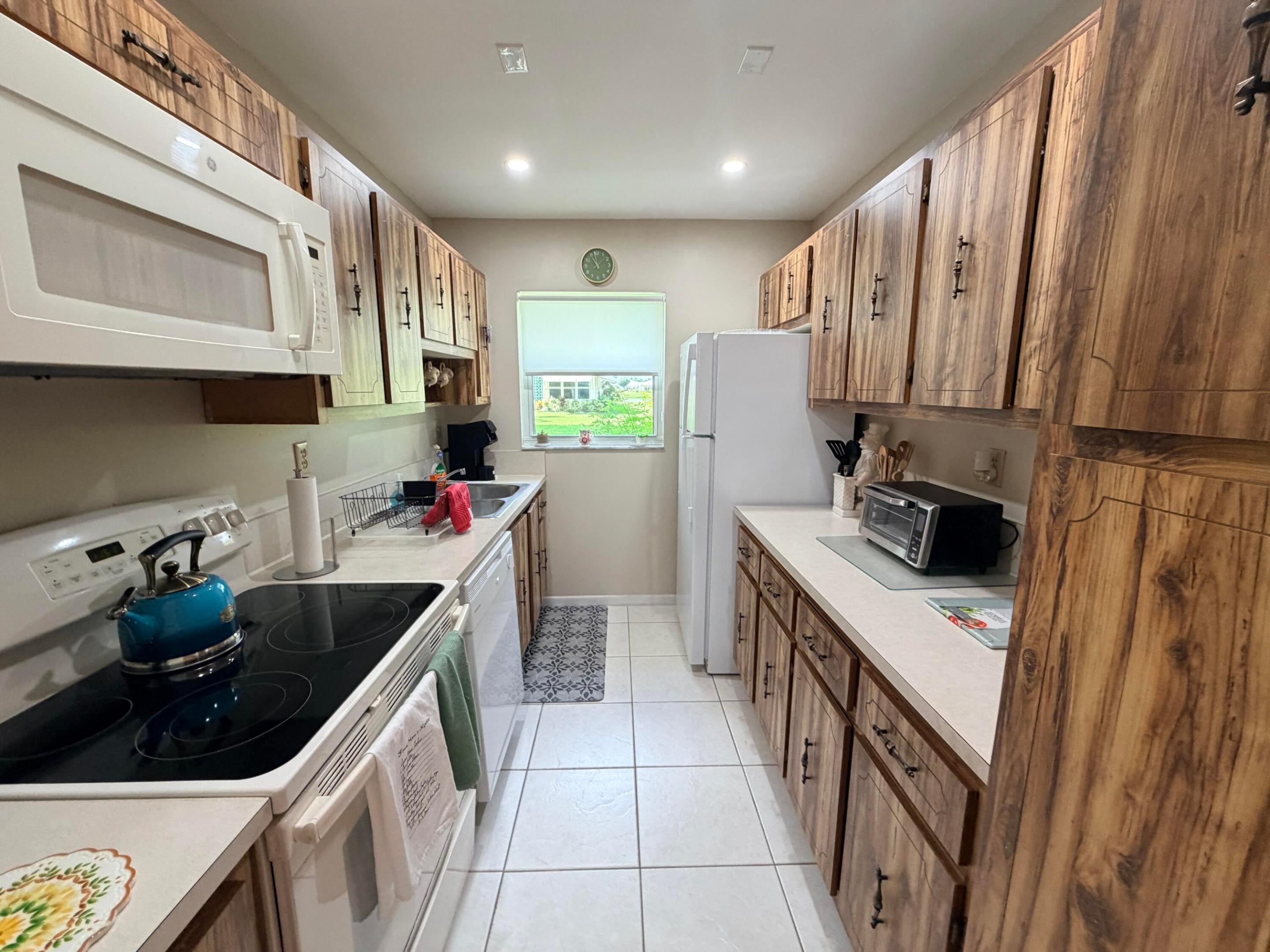 Galley kitchen with wood-grain cabinets, white appliances, and a blue kettle on the range.