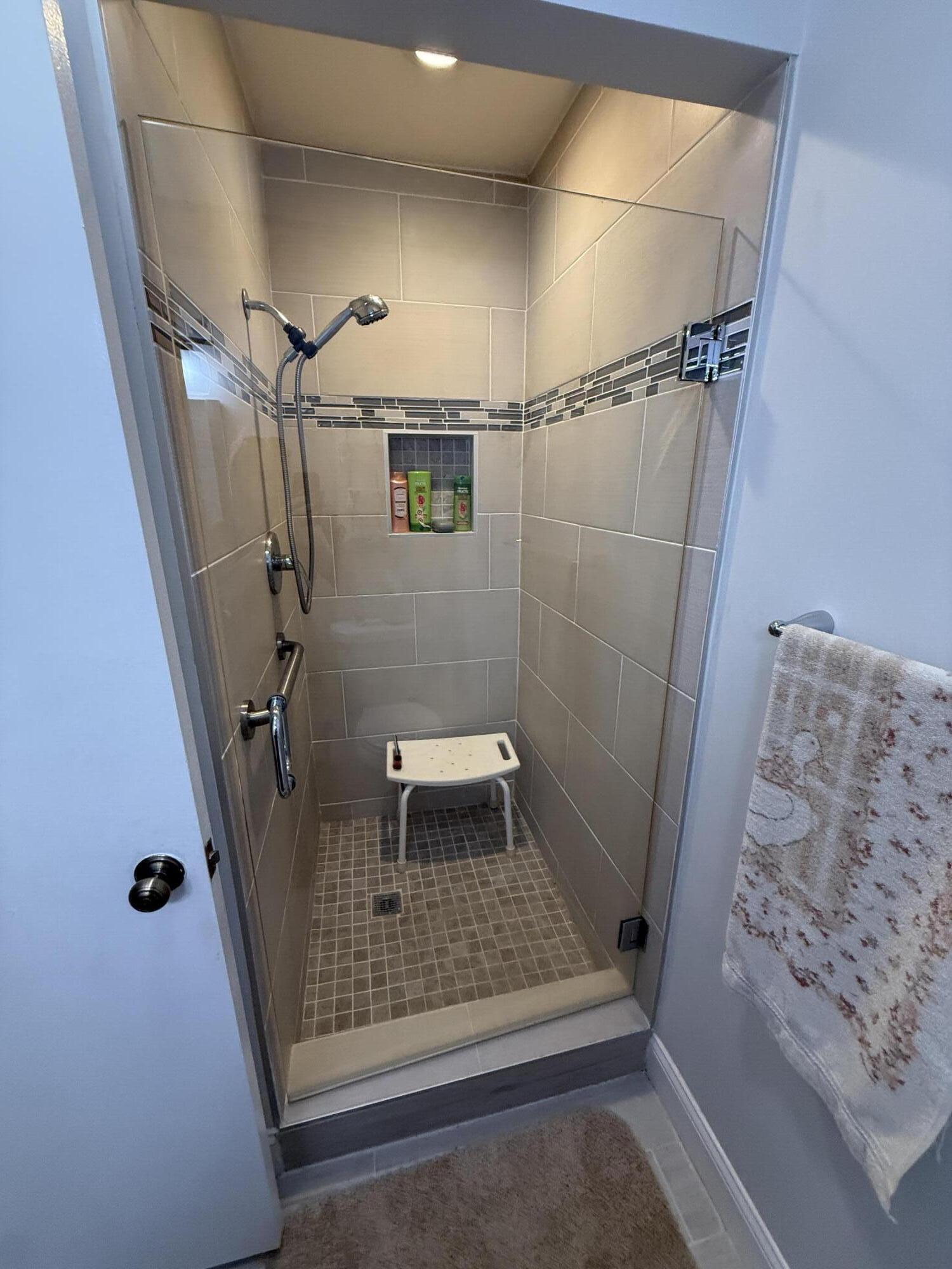 Walk-in tiled shower with grab bars, handheld showerhead, recessed niche, and shower seat.