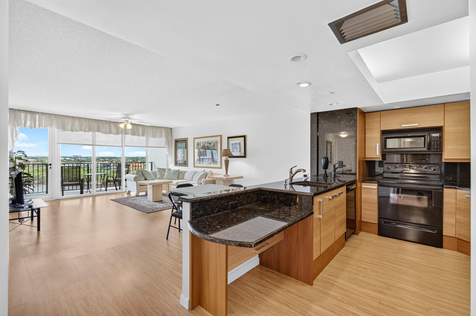 Open-plan kitchen and living room with granite island and floor-to-ceiling windows opening to a balcony.