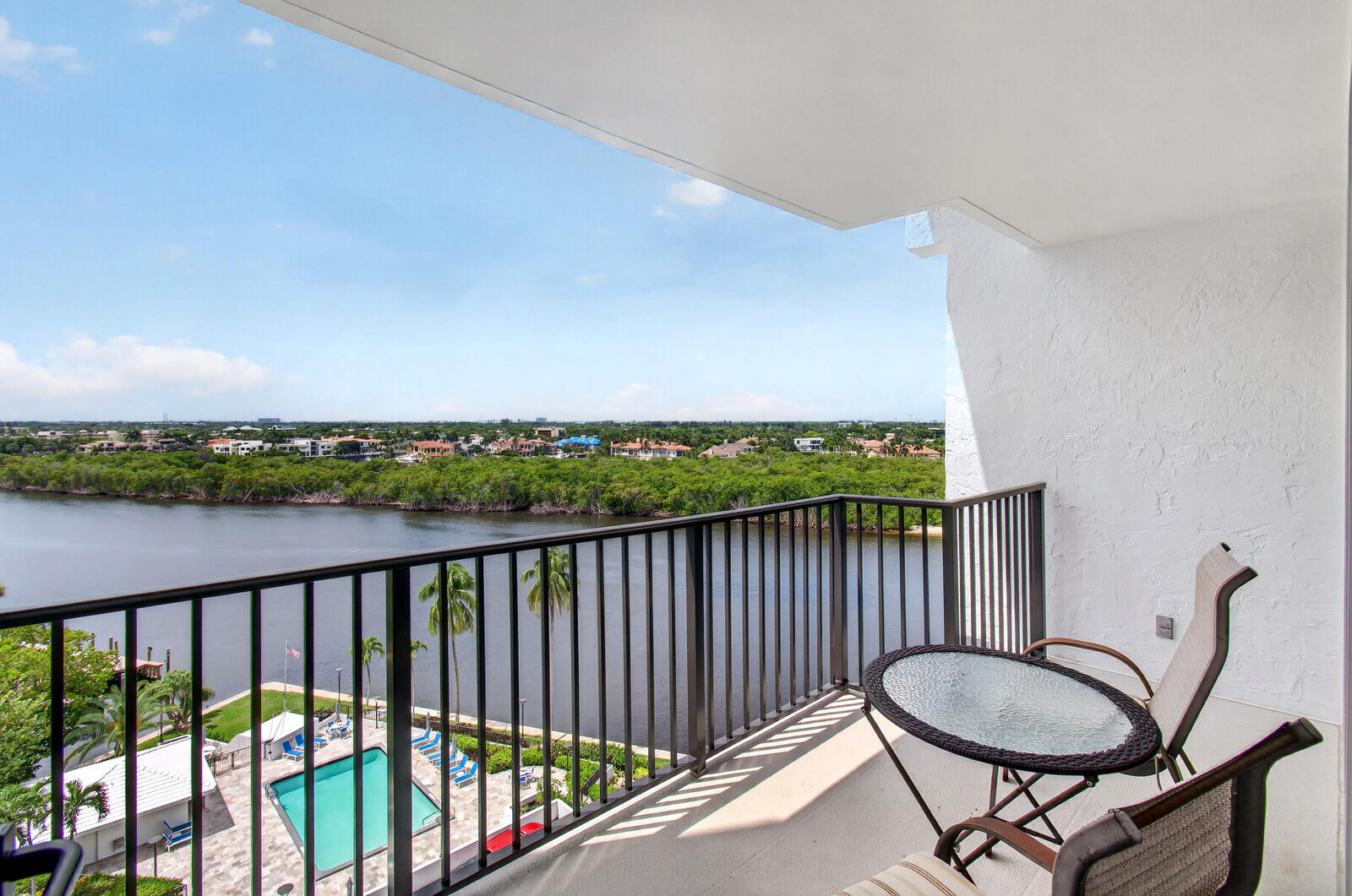 Apartment balcony with lounge chairs and a round table overlooking a waterway and pool.