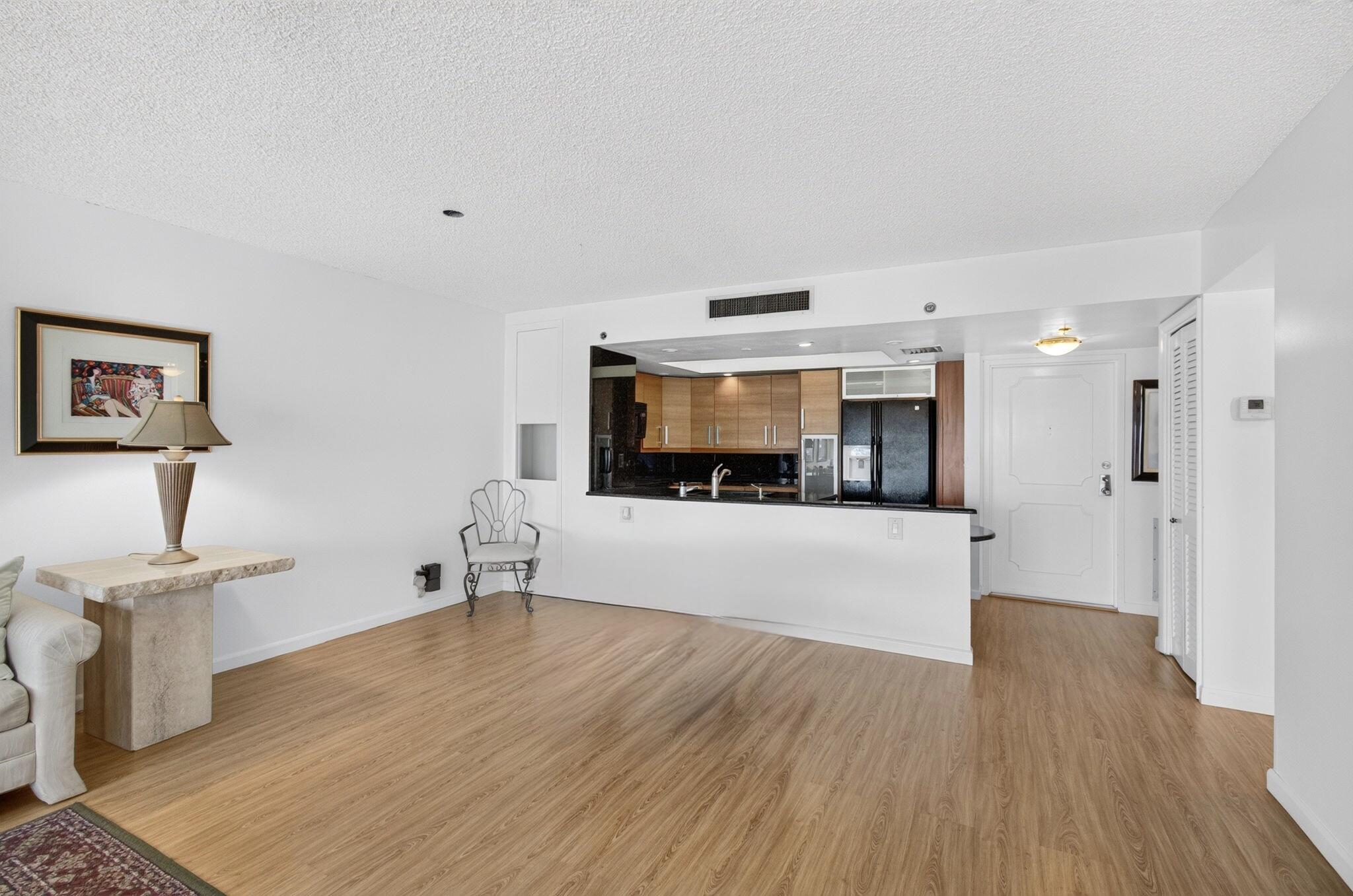 Condo living area with wood-look flooring, kitchen pass-through, and entry door.