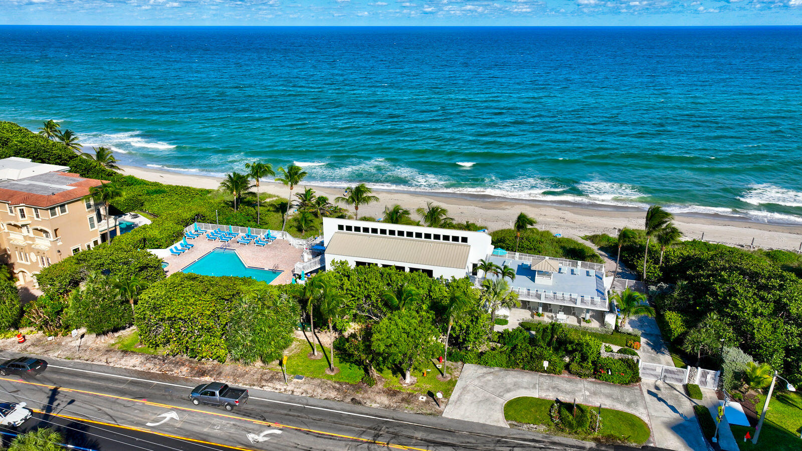 Aerial view of a beachfront property with a pool, palm trees, sandy beach, and ocean.