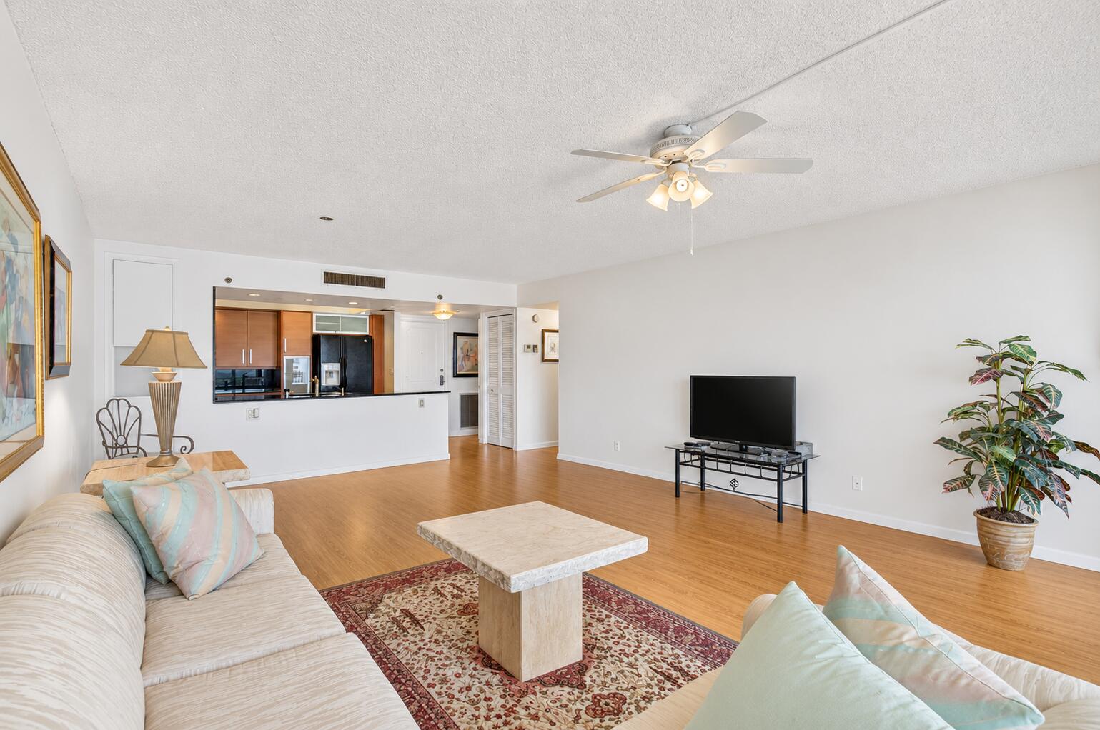 Living room with hardwood floors, light sofas, patterned rug, and an open kitchen.