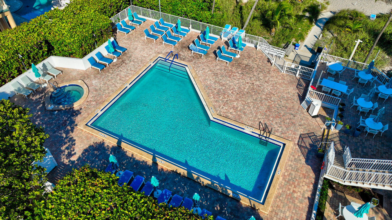 Aerial view of a large pool and round spa surrounded by blue loungers and a brick-paved deck.