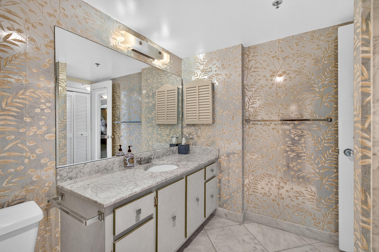 Bathroom with a marble vanity and mirror, accented by gold botanical wallpaper.