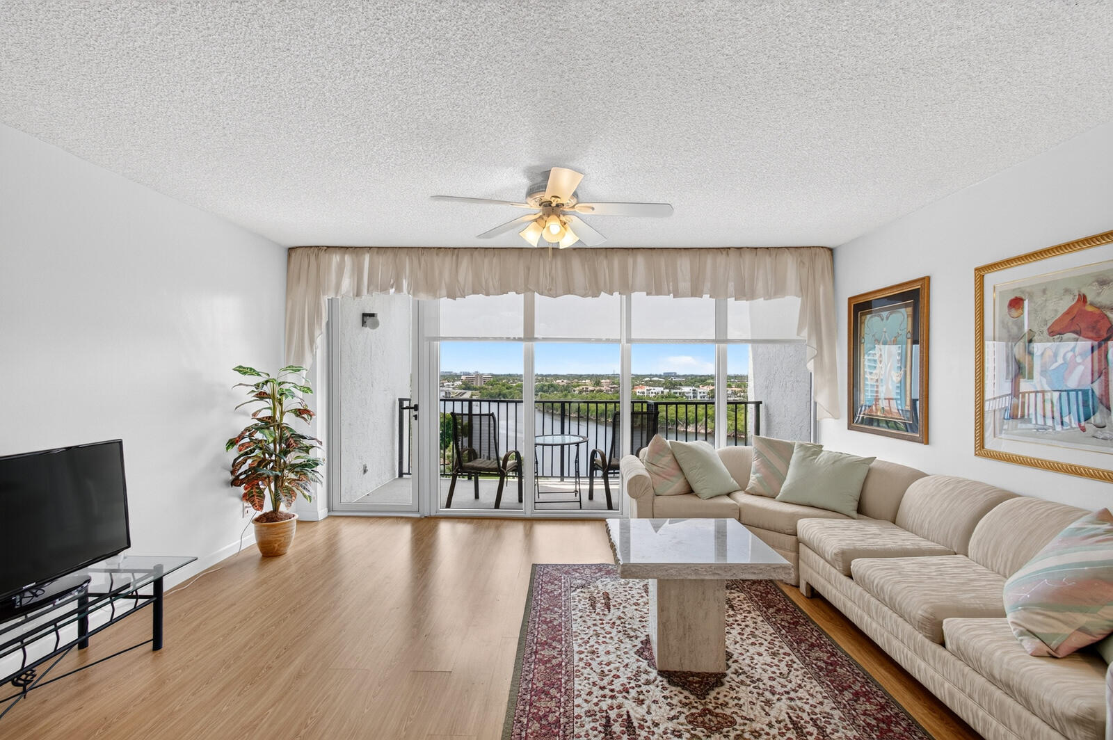 Furnished living room with a cream sectional and balcony overlooking the water.