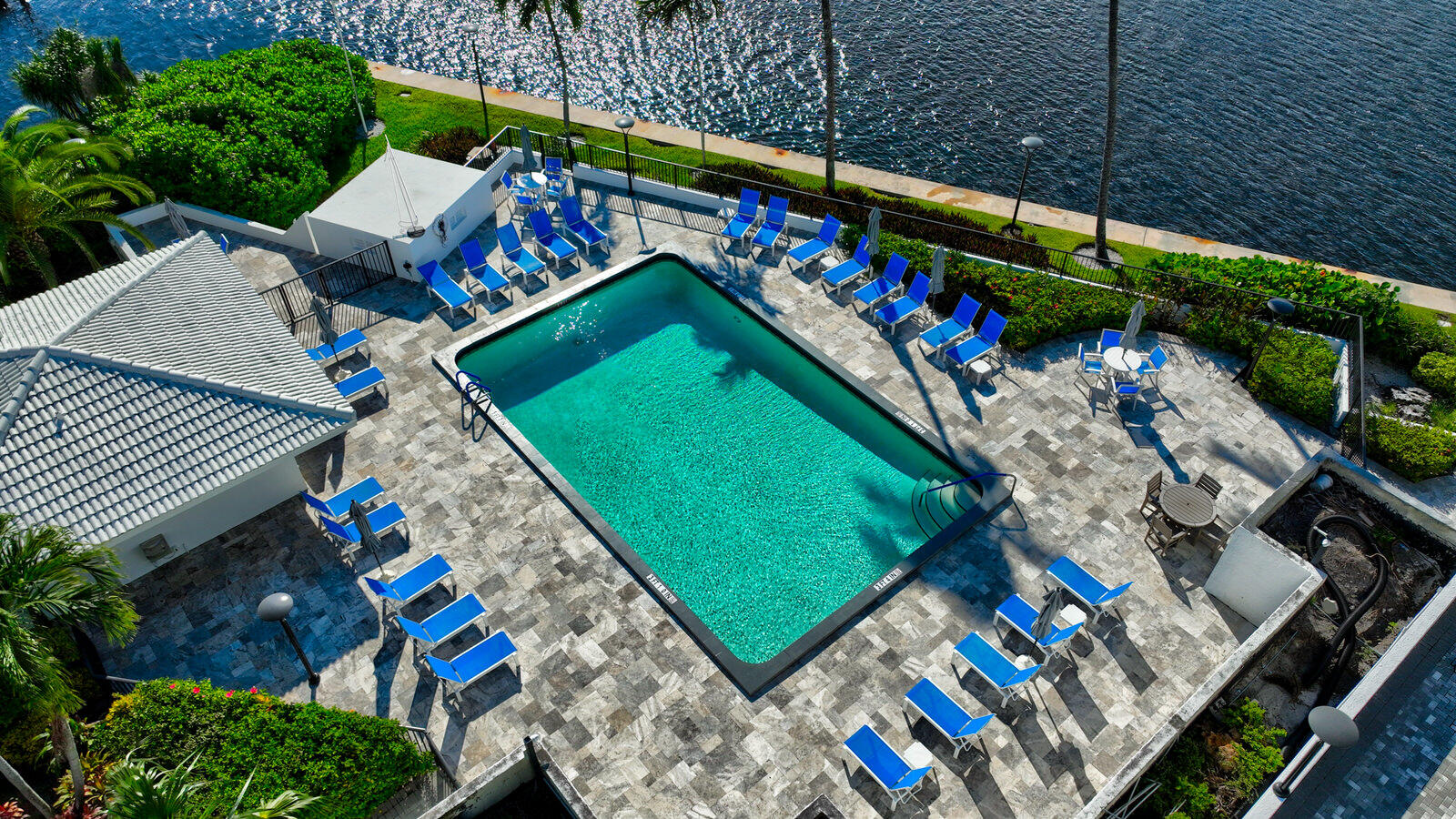 Aerial view of a turquoise pool surrounded by blue lounge chairs beside the waterfront.