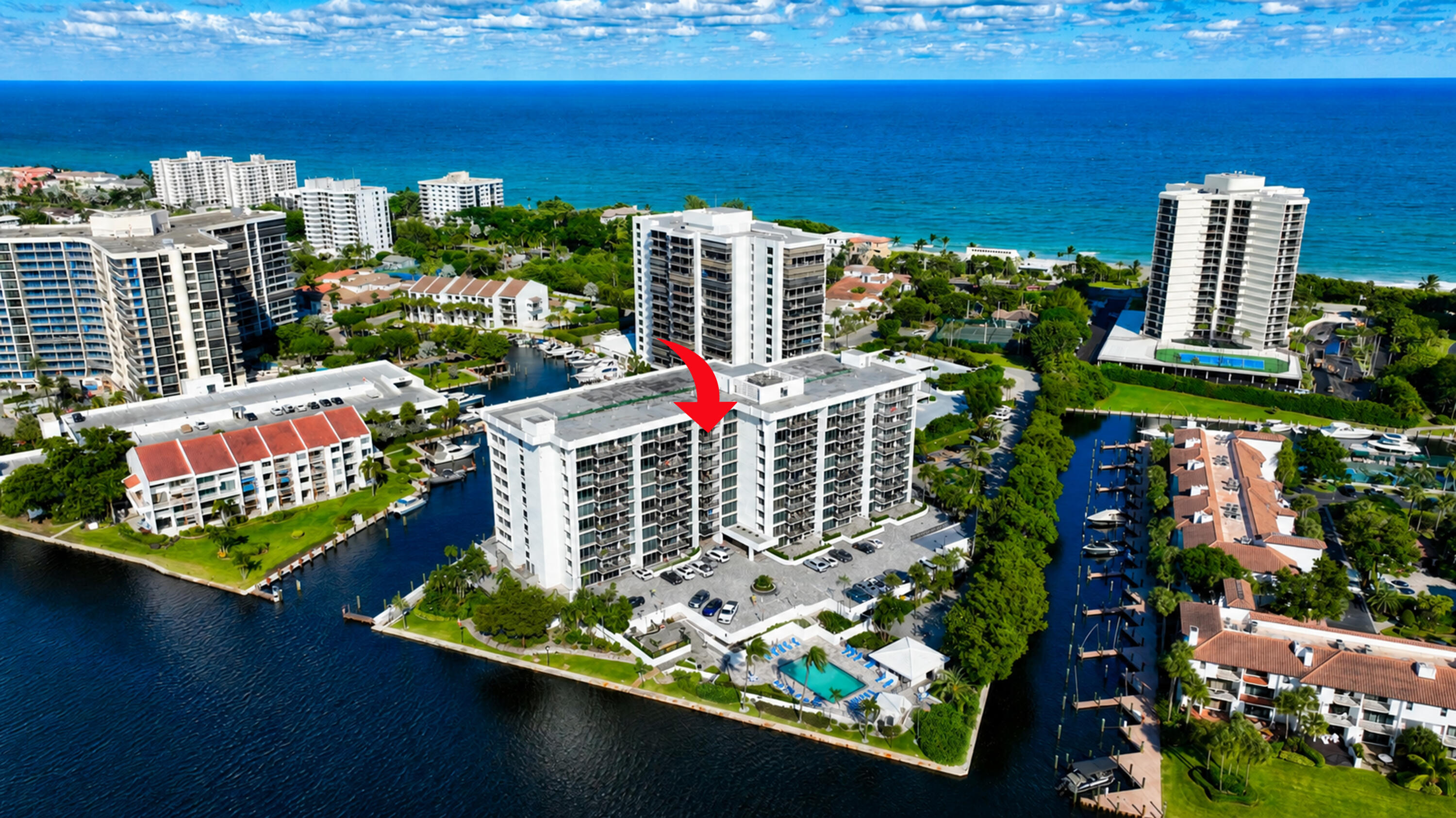 Aerial view of a waterfront condominium complex, marked by a red arrow, with canals and ocean beyond.