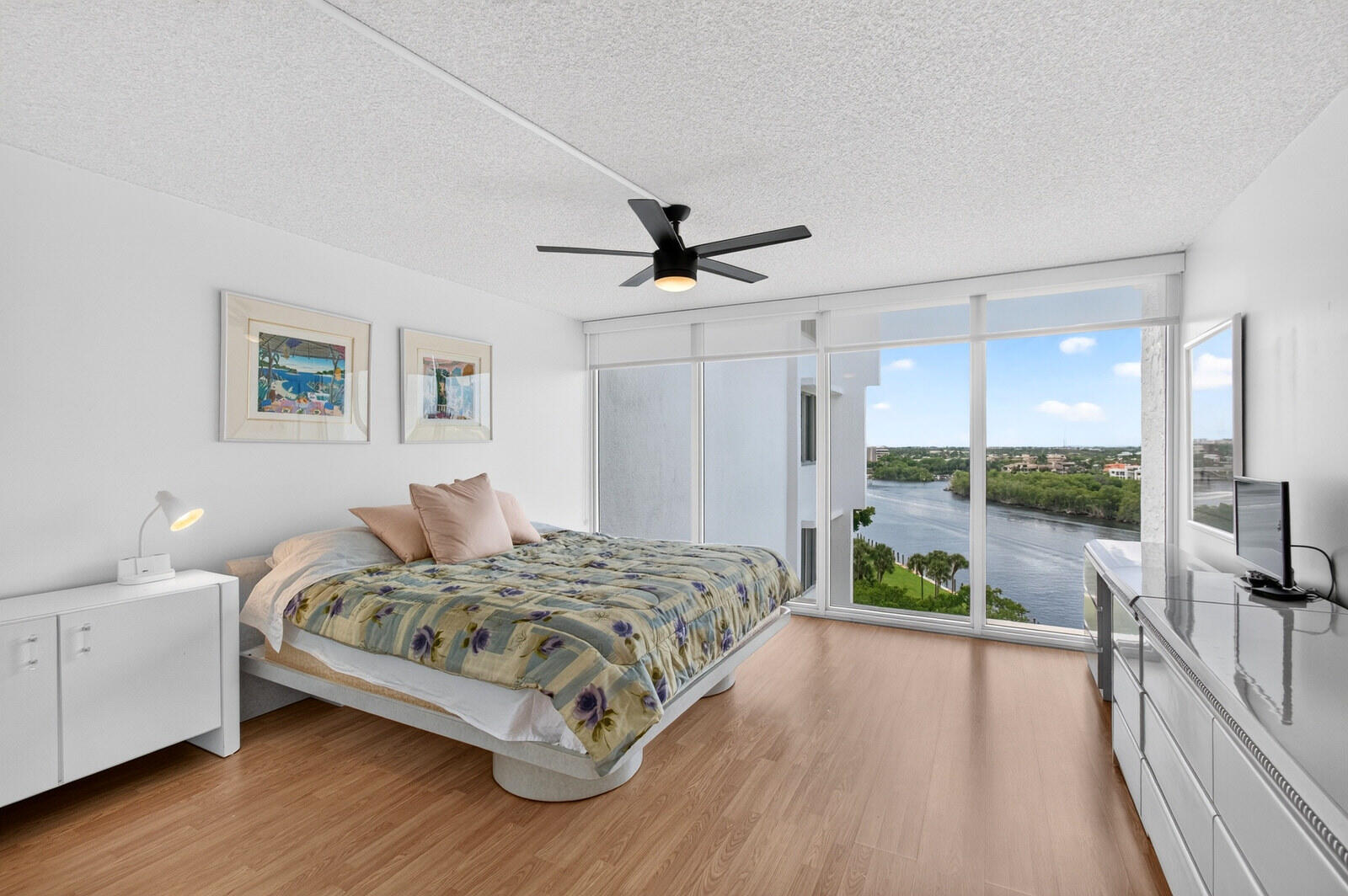 Bedroom with sliding glass doors overlooking a waterway and green shoreline.