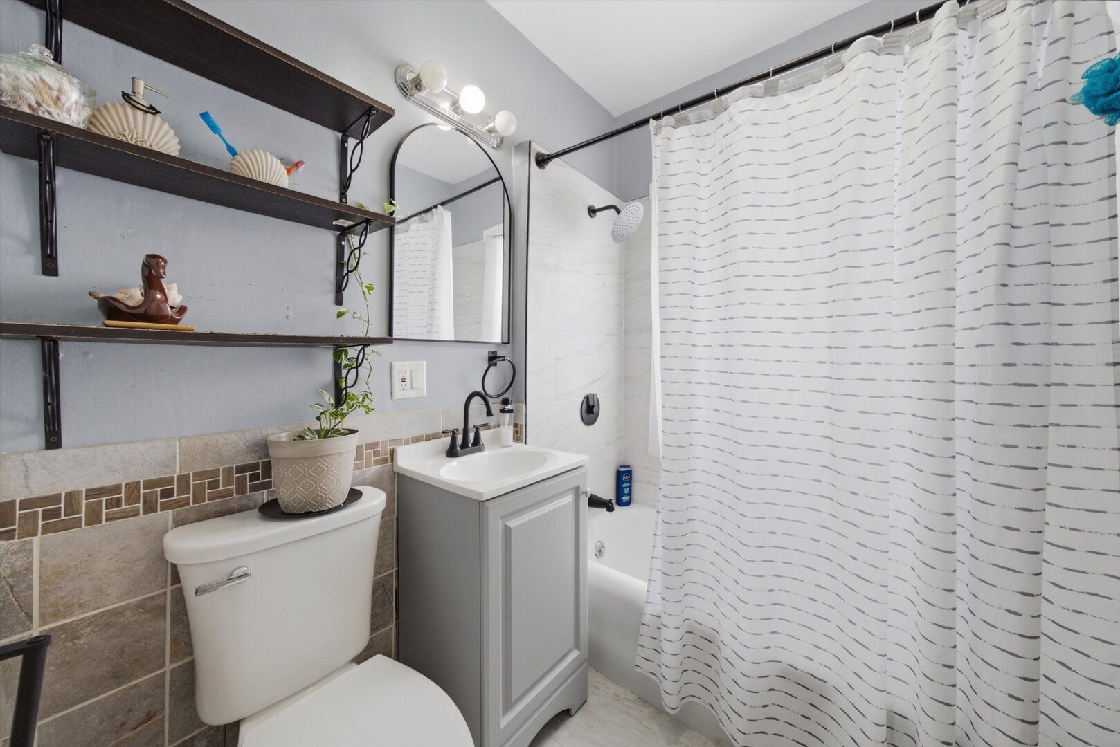 Bathroom with a gray vanity, tiled walls, open shelves, and a white striped shower curtain.