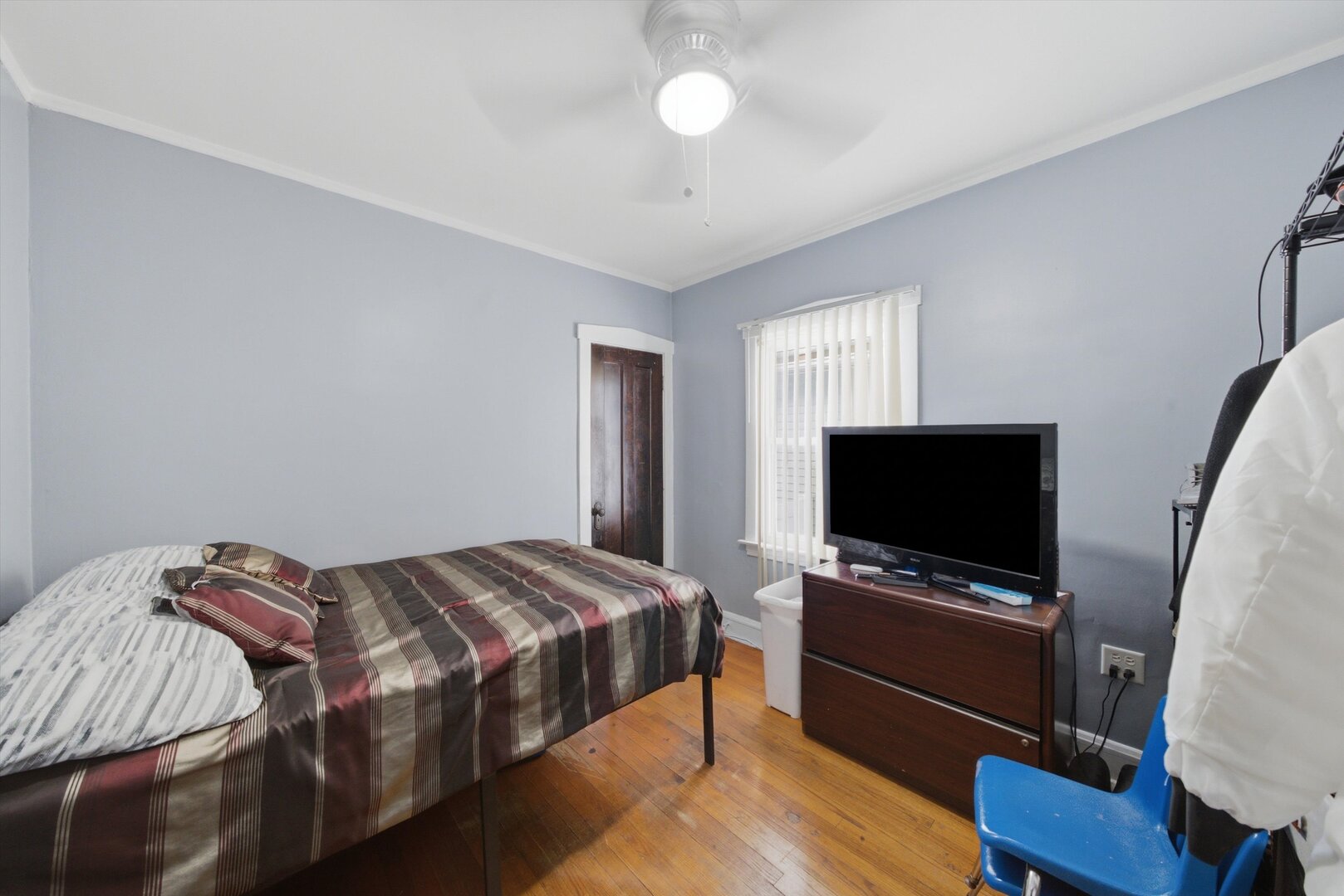 Bedroom with striped bedding, hardwood floors, and a television on a wooden dresser.