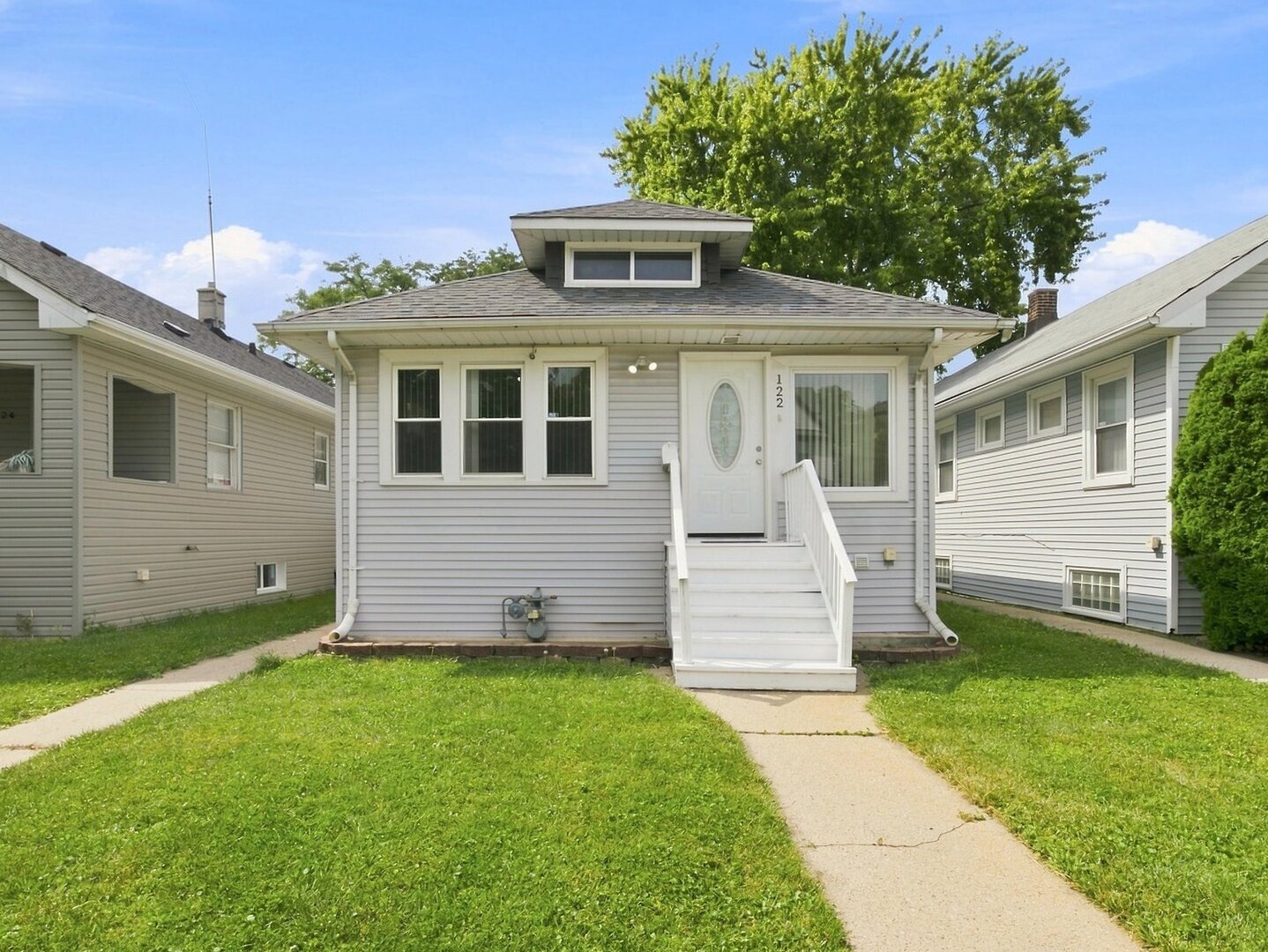 Gray-sided house with a centered entry staircase, front dormer, and small lawn.