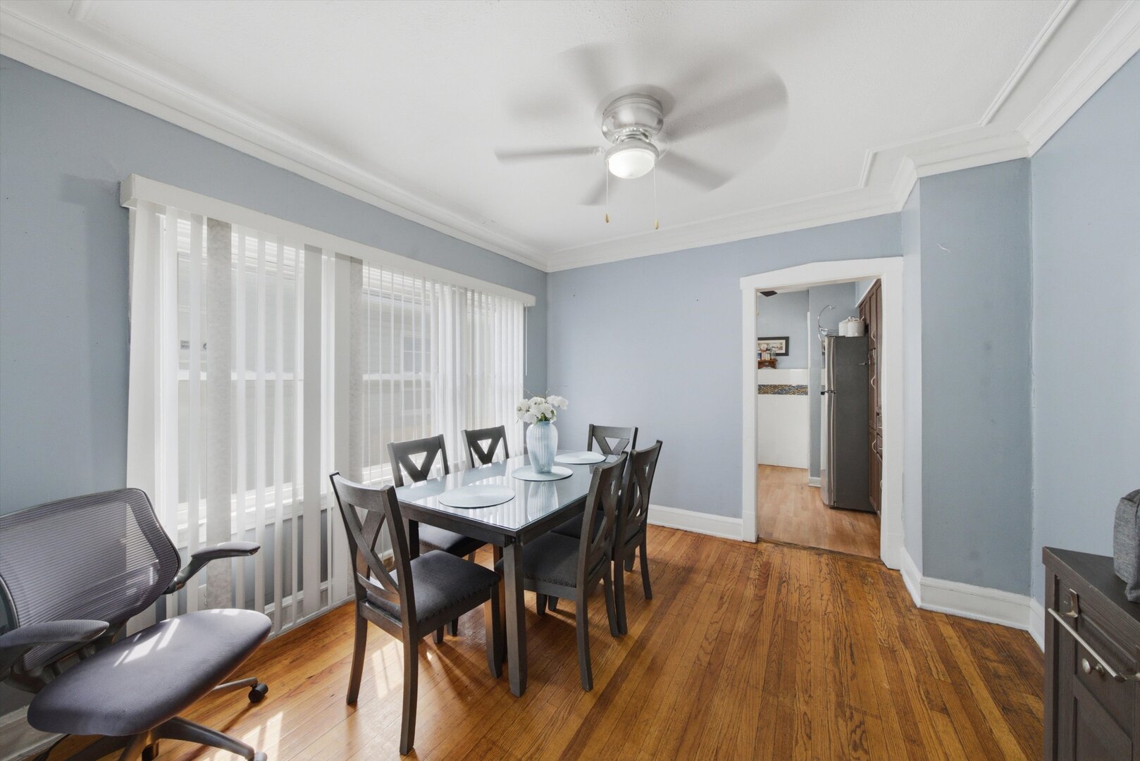 Dining room with a dark table, polished hardwood floors, wide windows with vertical blinds, and a ceiling fan.