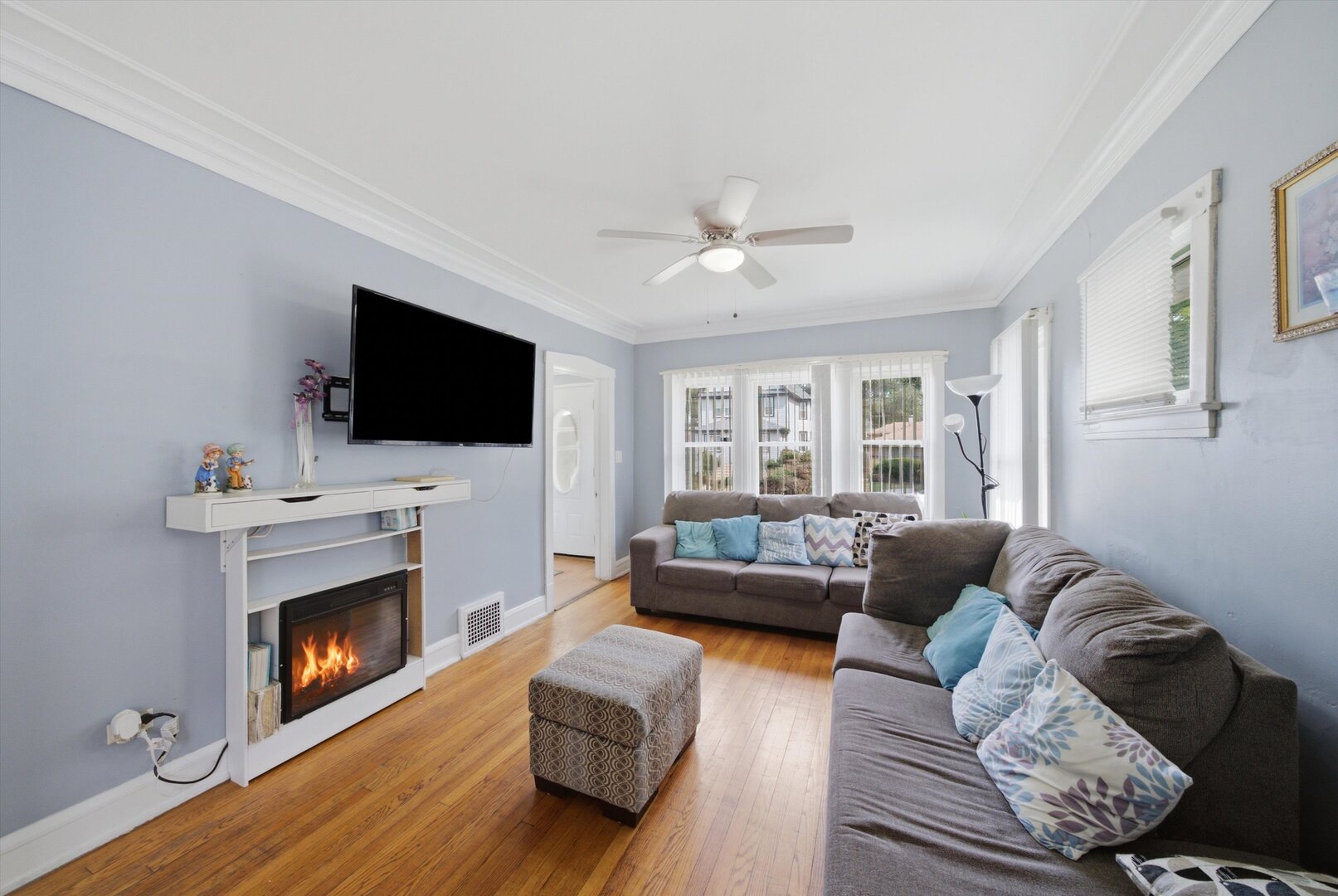 Living room with hardwood floors, gray sofas, a fireplace, and wide windows.