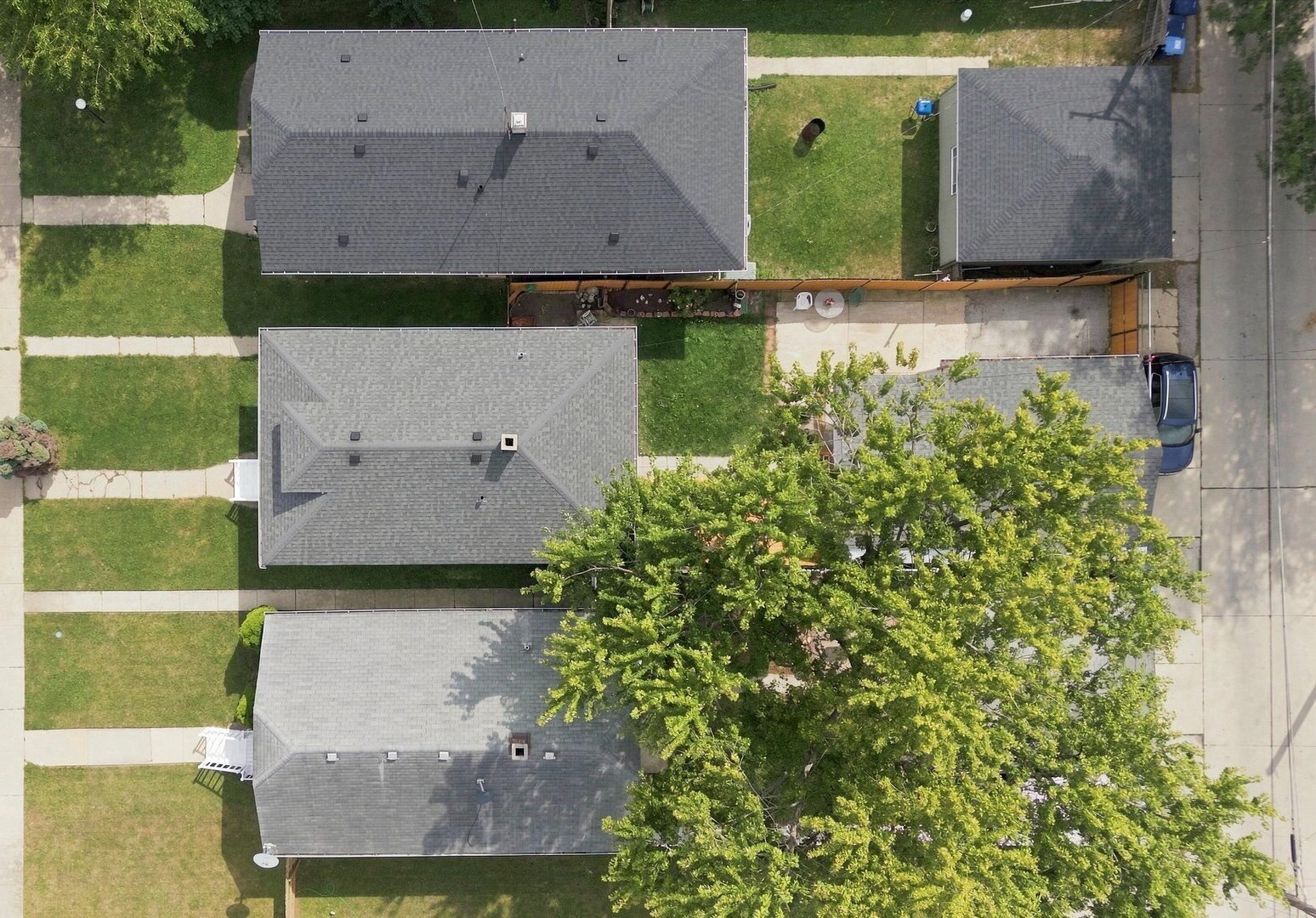 Aerial view of a gray-roofed home with a lawn, paved patio, and detached garage.