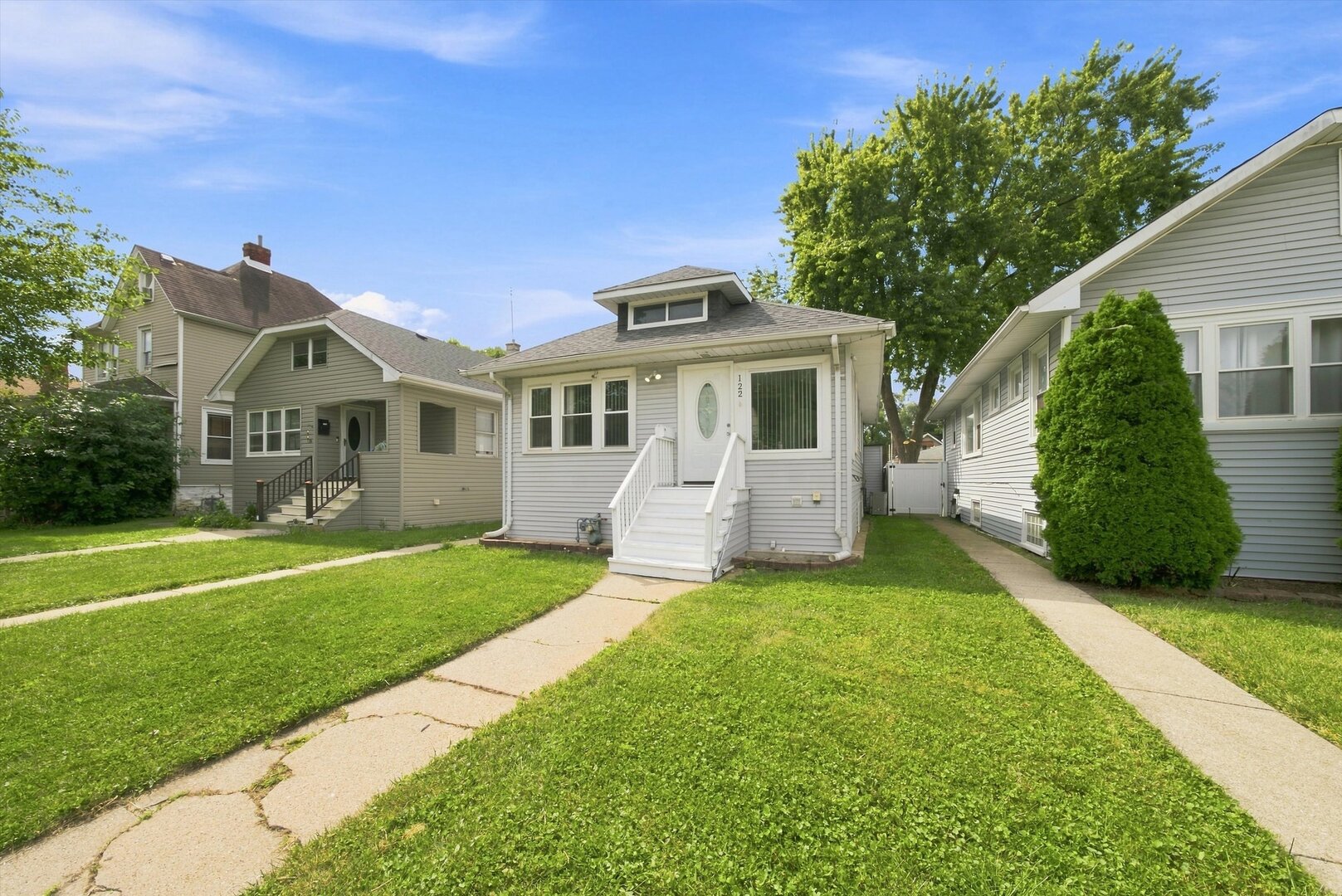 Light-gray house with white front steps, a green lawn, and neighboring homes.