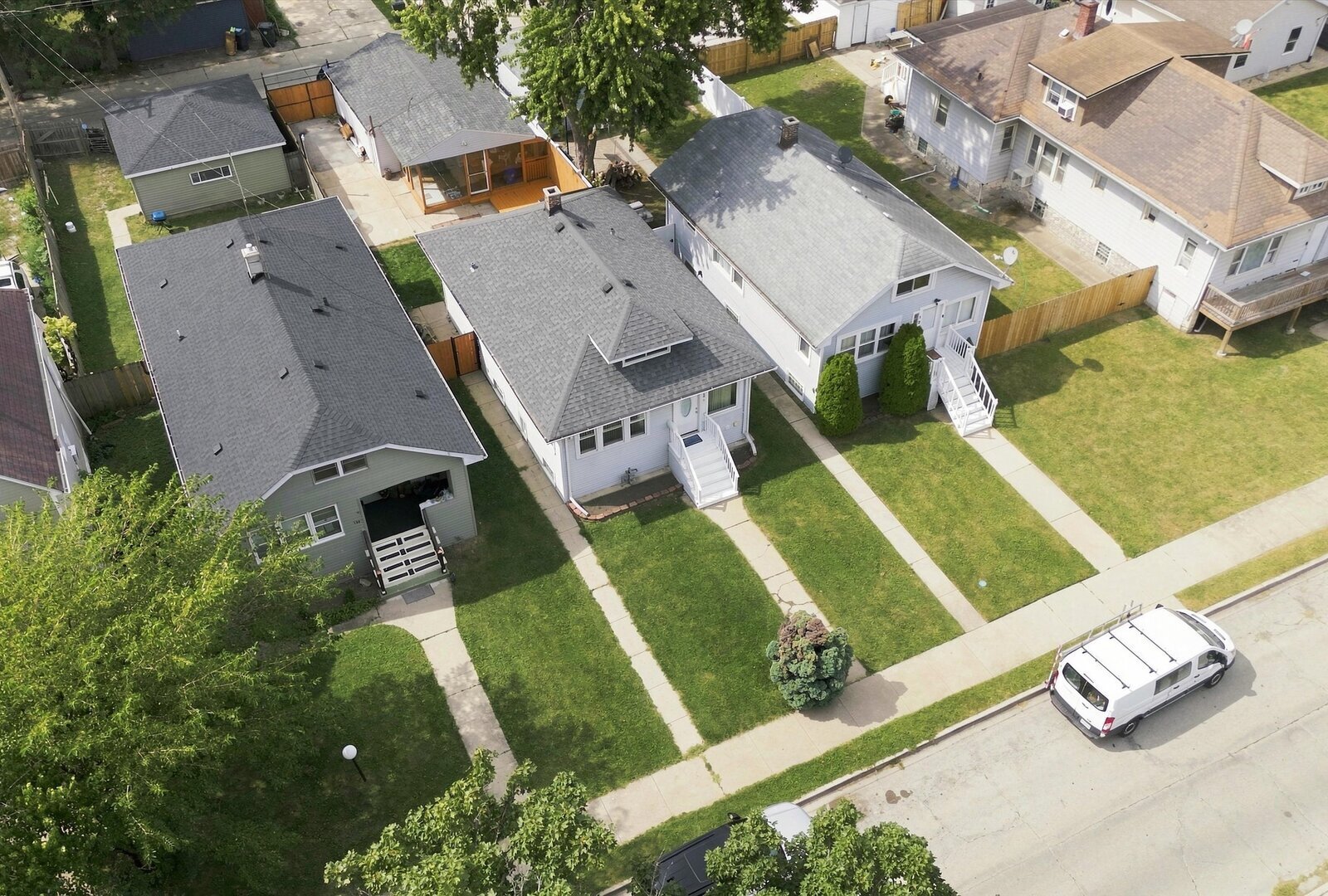 Aerial view of a white-sided home with a gray roof, front steps, and neighboring houses.