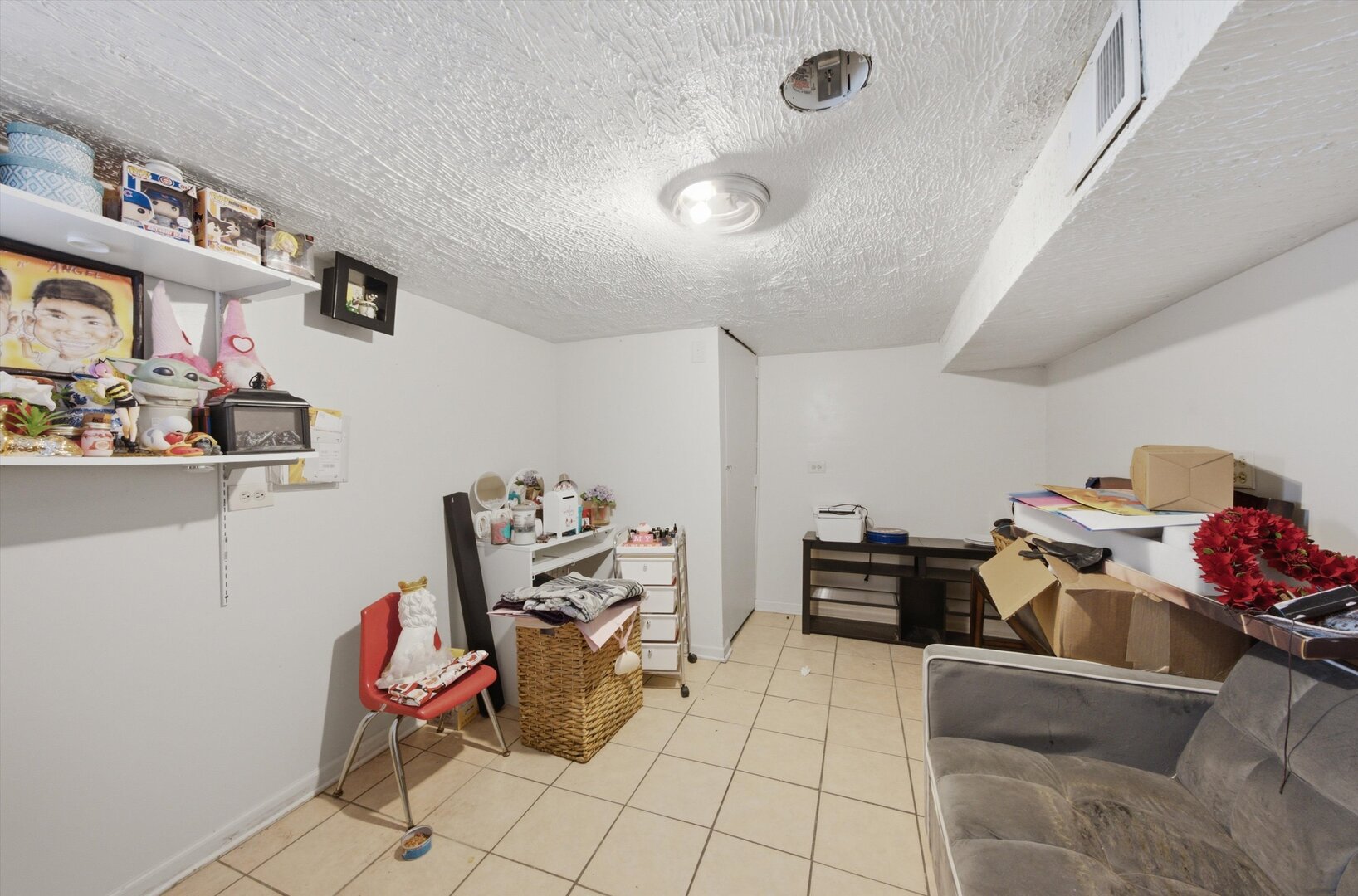 Basement room with a low ceiling, tiled floor, wall shelves, and a gray sofa.