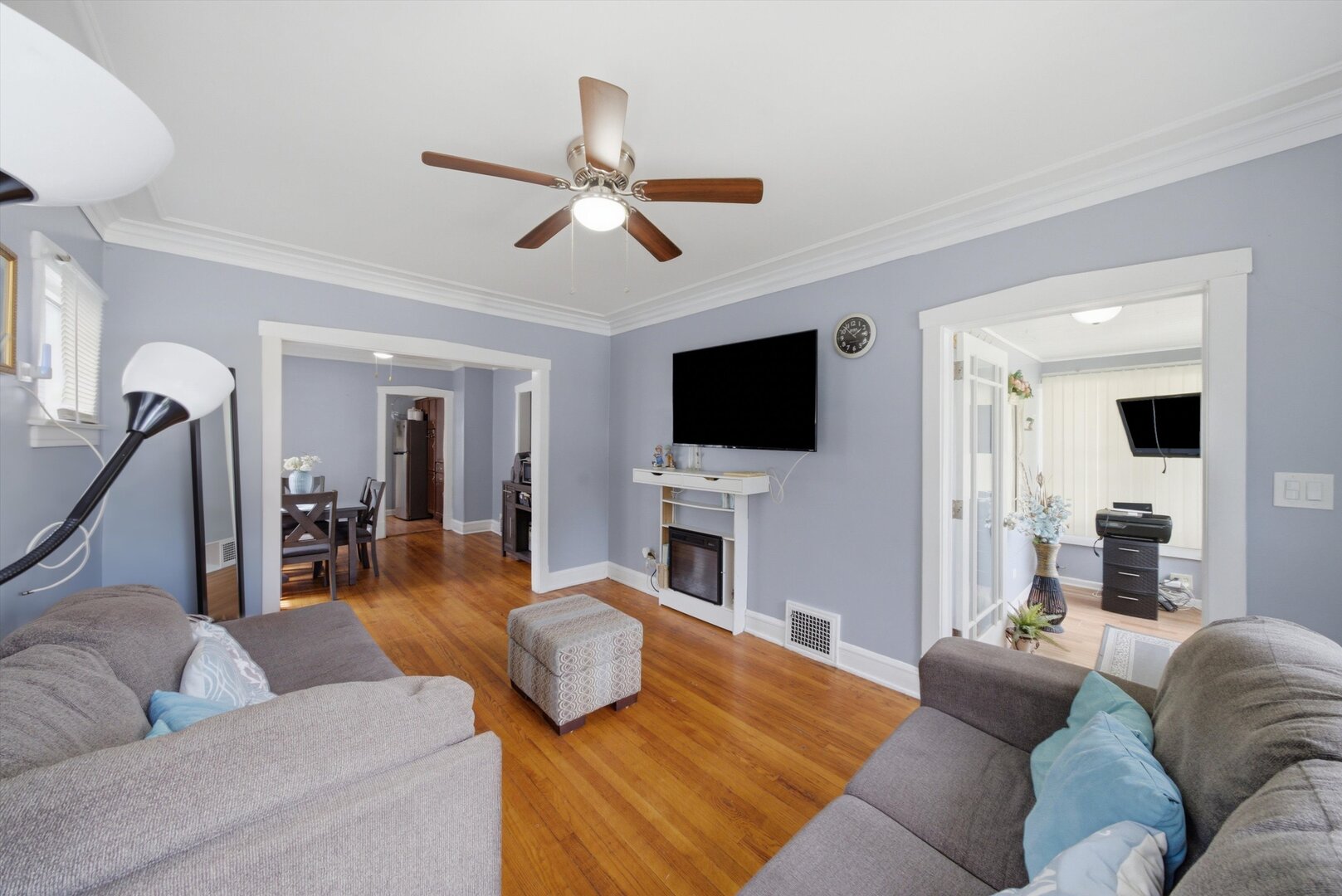 Furnished living room with hardwood floors, pale blue walls, and a fireplace beneath a mounted TV.