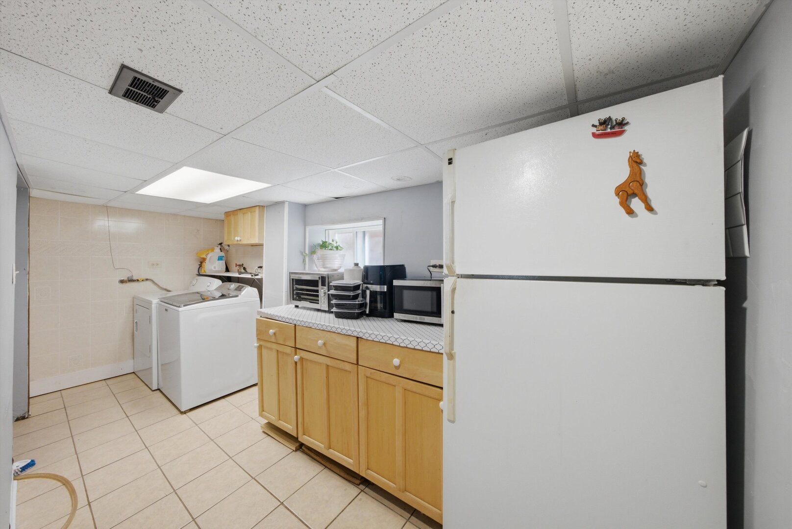 Laundry room with a washer and dryer beside wood cabinets and a large refrigerator.