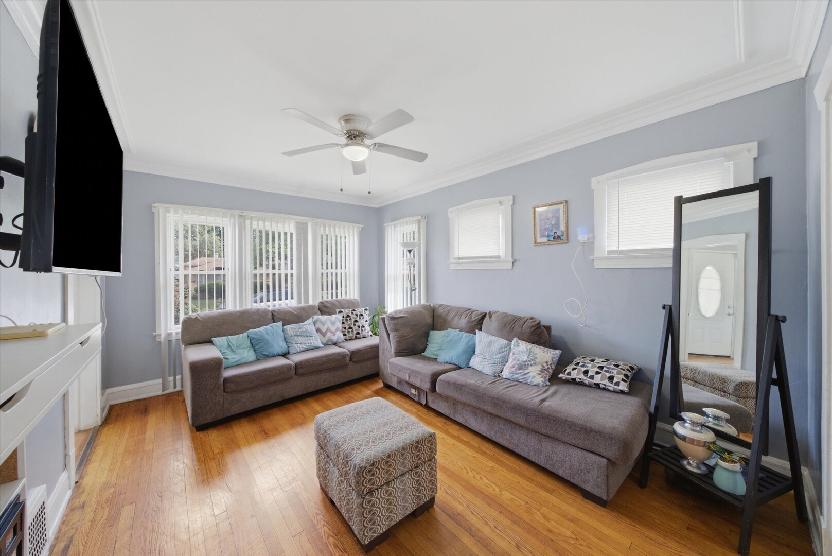 Living room with gray sectional sofas, hardwood floors, and large windows with vertical blinds.