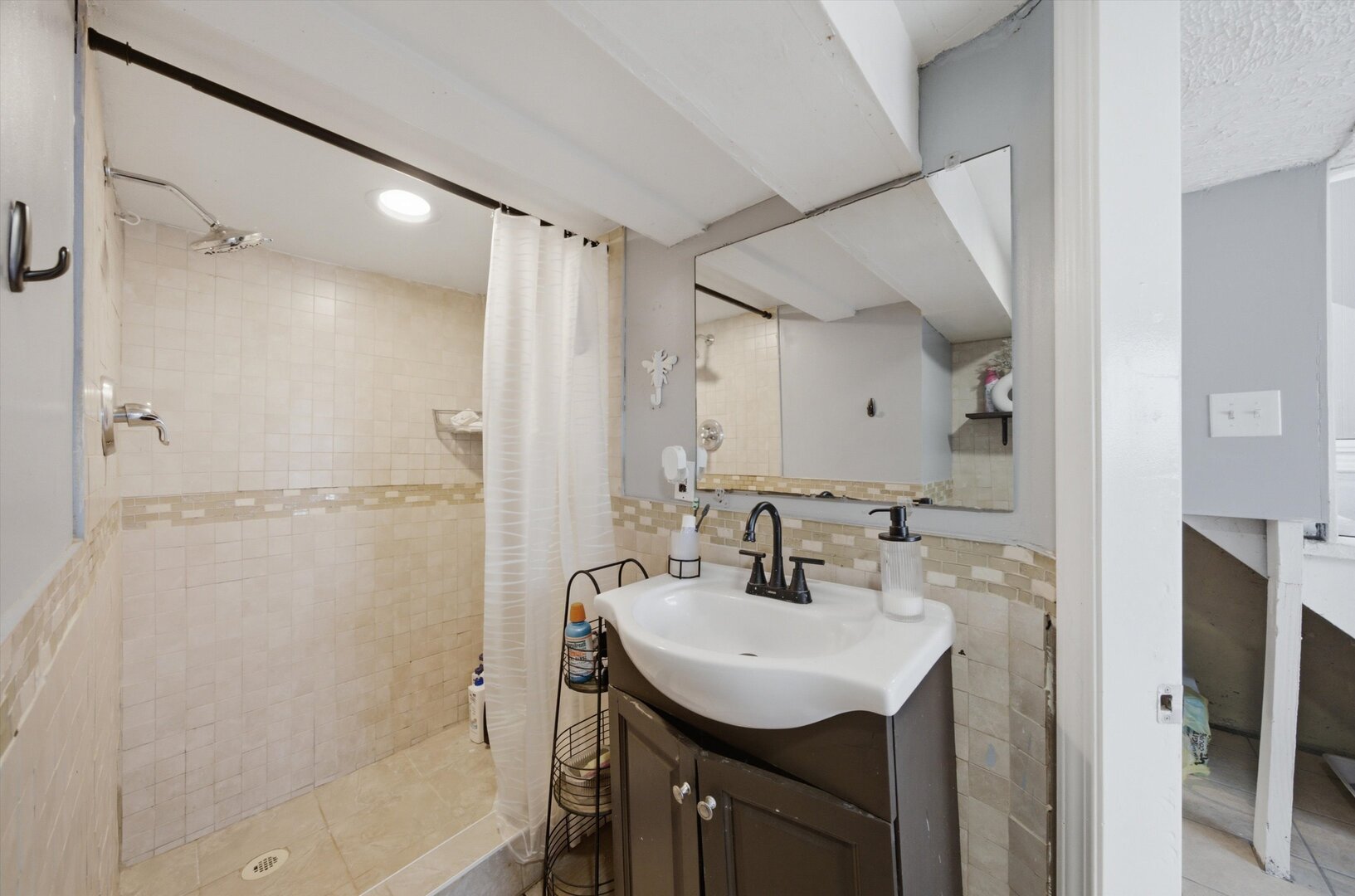 Bathroom with a tiled walk-in shower, white curtain, and dark vanity beneath a large mirror.