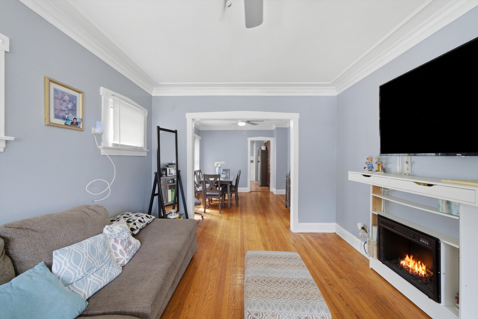 Living room with hardwood floors, a gray sectional, and an electric fireplace beside the dining room.