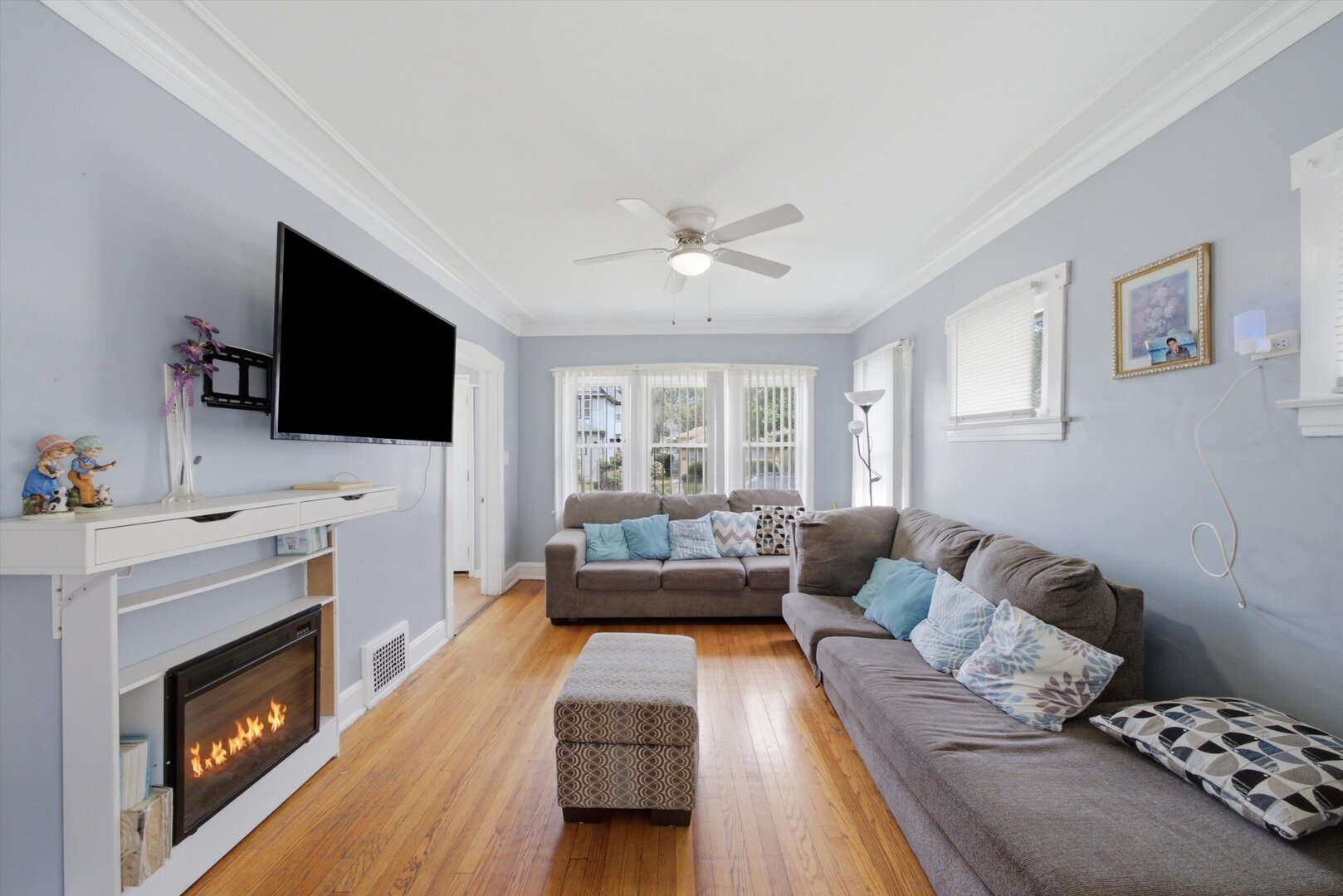 Living room with hardwood floors, gray sectional, and an electric fireplace beneath a wall-mounted TV.