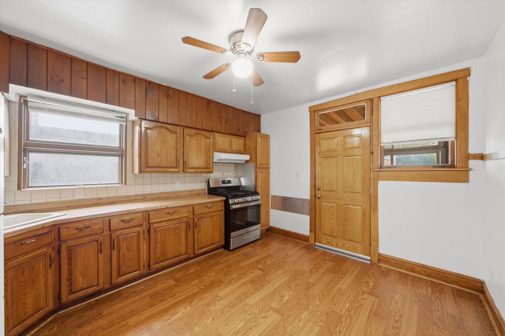 Vacant kitchen with honey-toned wood cabinets, hardwood floors, and a wood-trimmed back door.