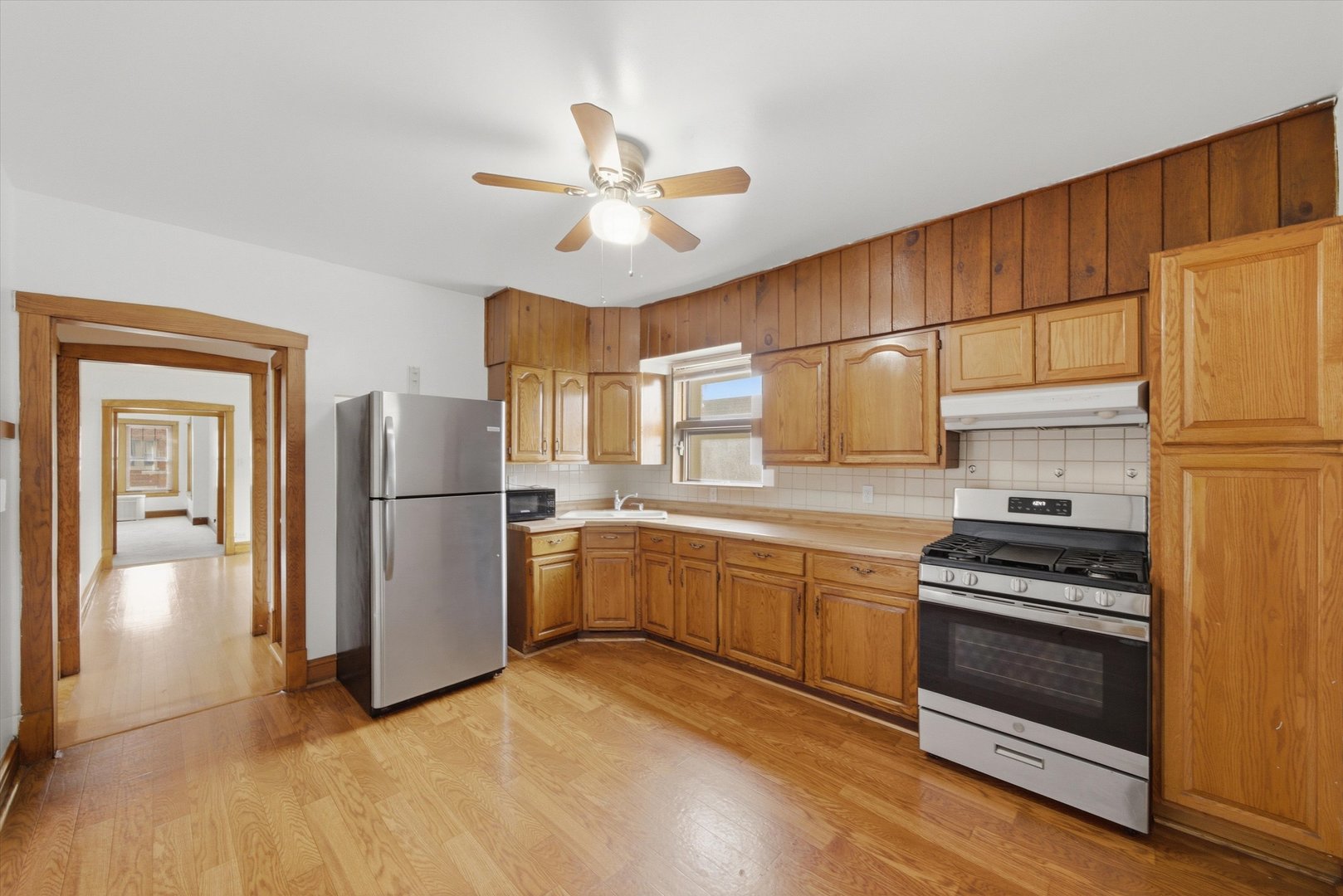 Kitchen with honey-colored wood cabinets, wood-paneled walls, and stainless steel appliances.