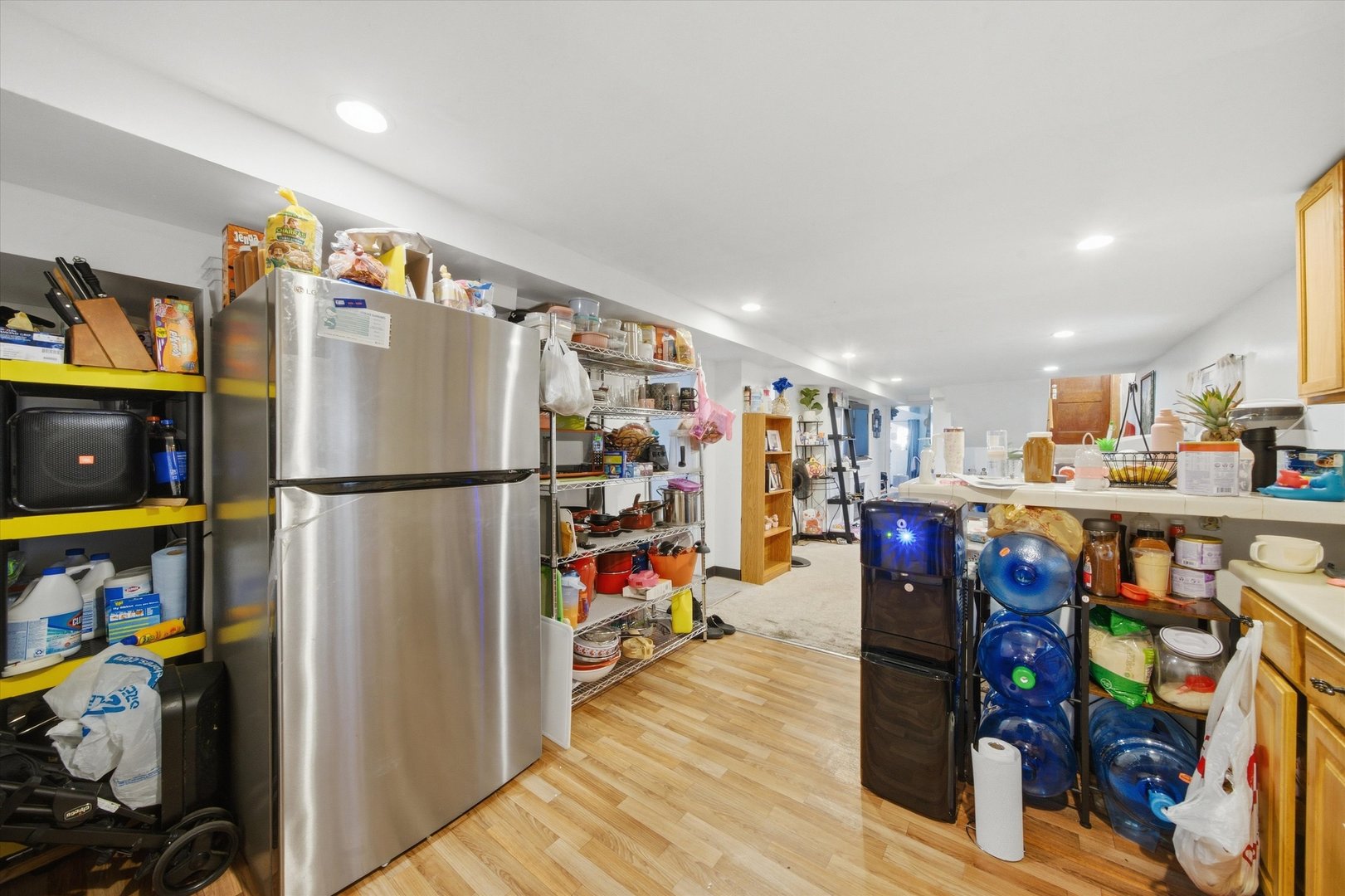 Kitchen with a stainless steel refrigerator, crowded open shelving, and light wood-look flooring.