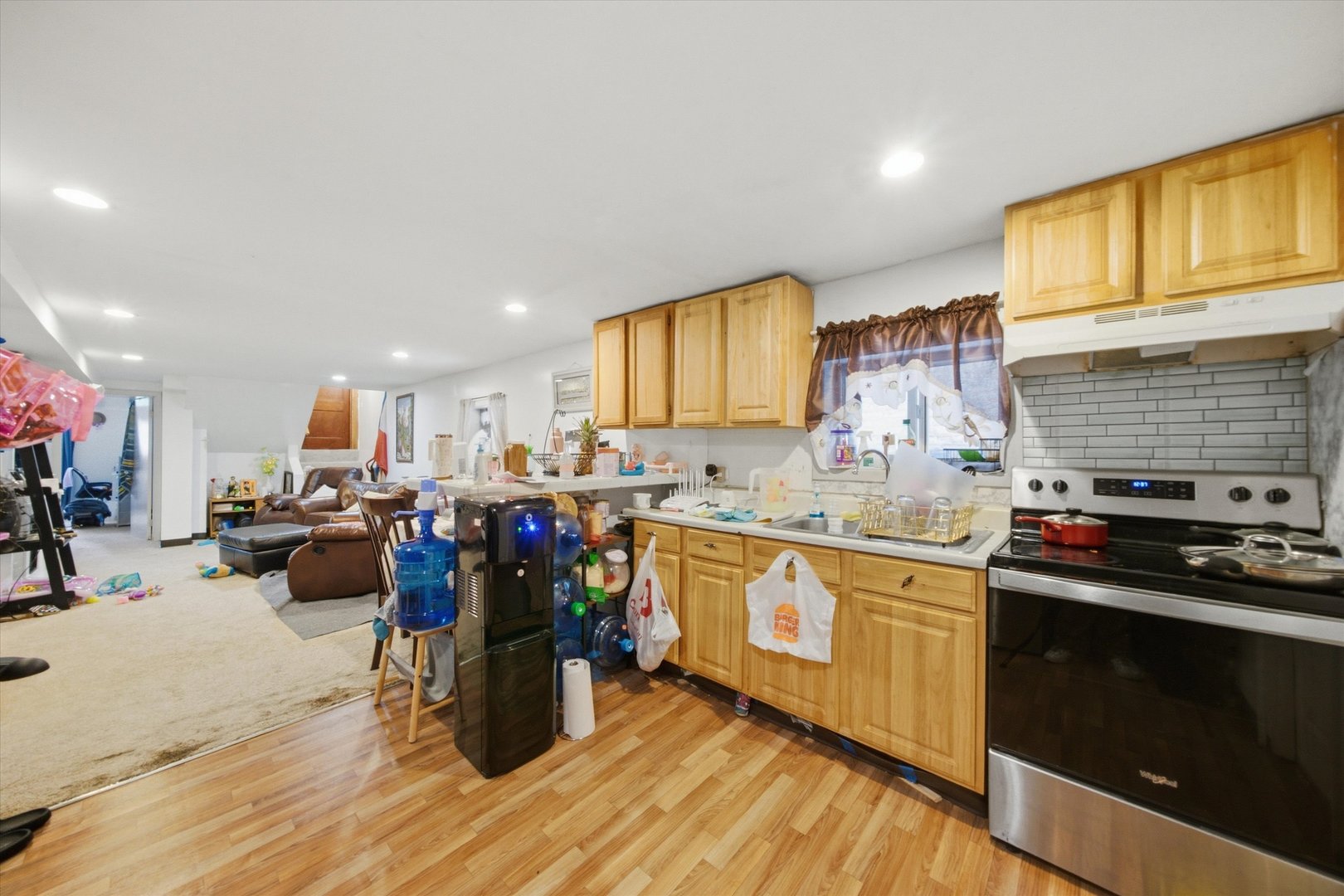 Kitchen with honey-colored cabinets and a stainless range, opening onto a carpeted living area.