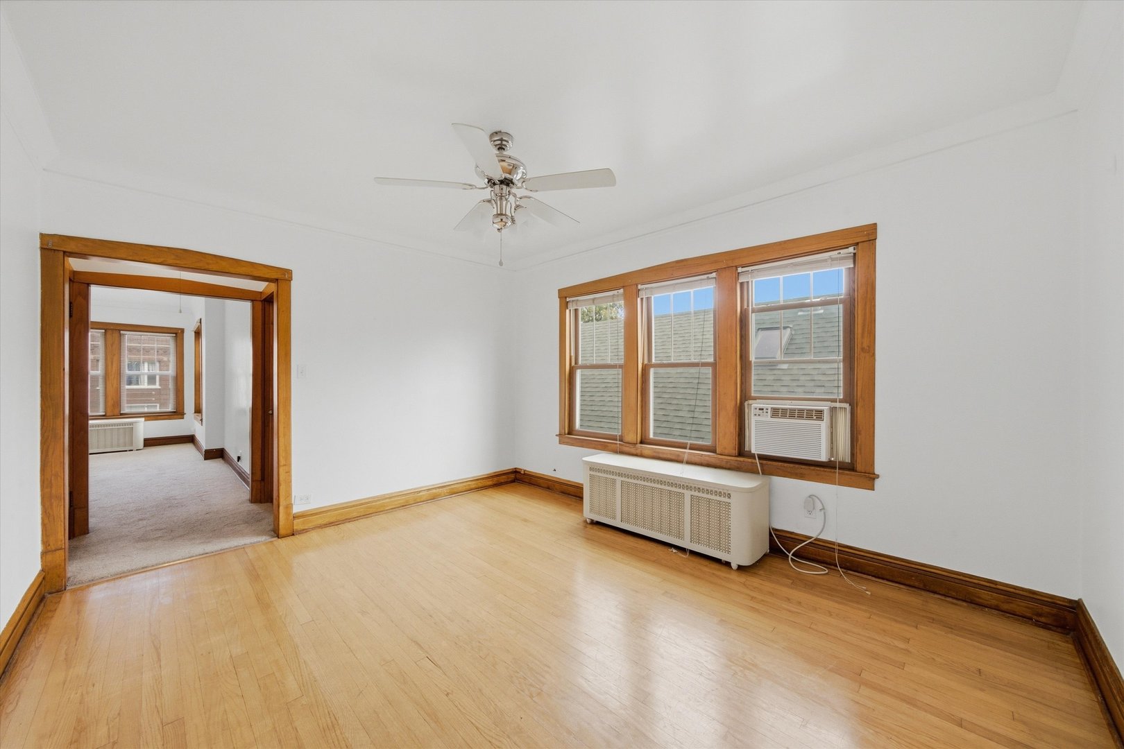 Empty room with hardwood floors, wood-trimmed windows, and a ceiling fan.