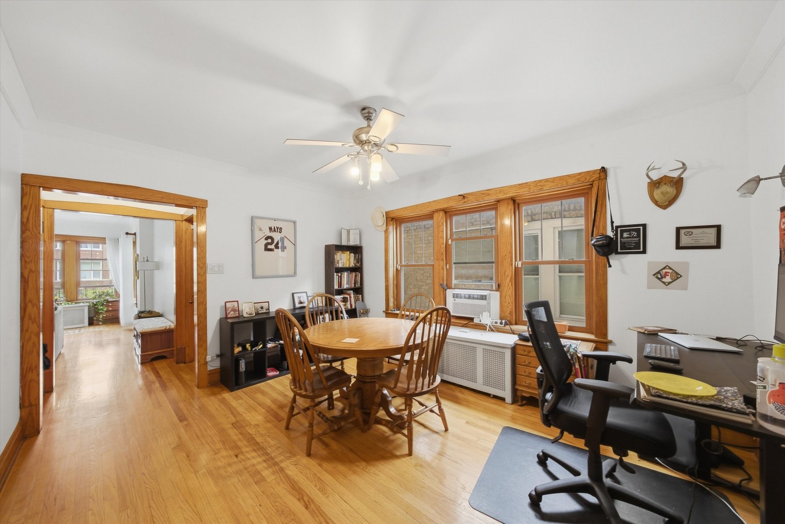 Dining room and home office with a round wooden table, hardwood floors, and wood-trimmed windows.