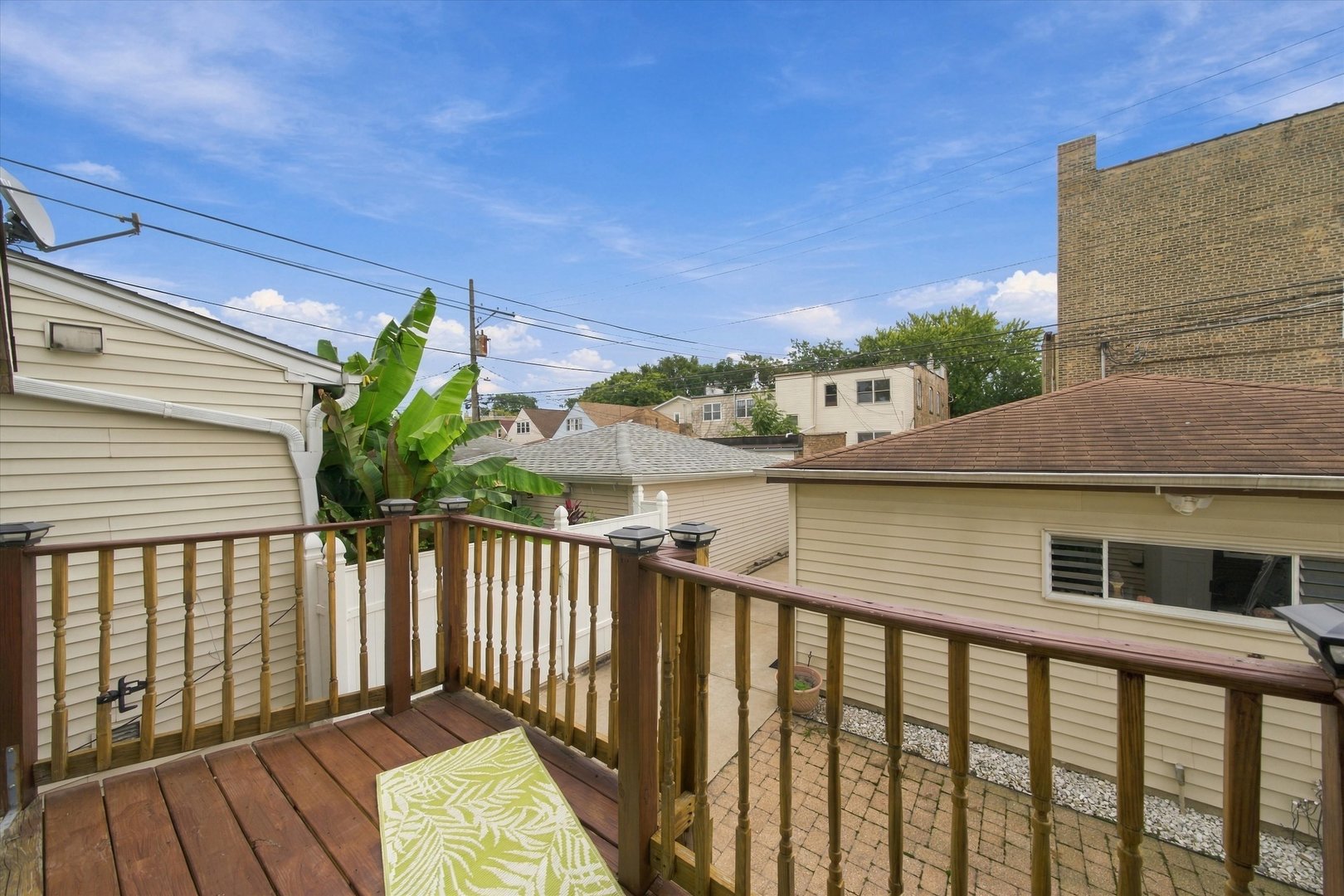 Wooden deck overlooking a paved patio, neighboring homes, and leafy plants.