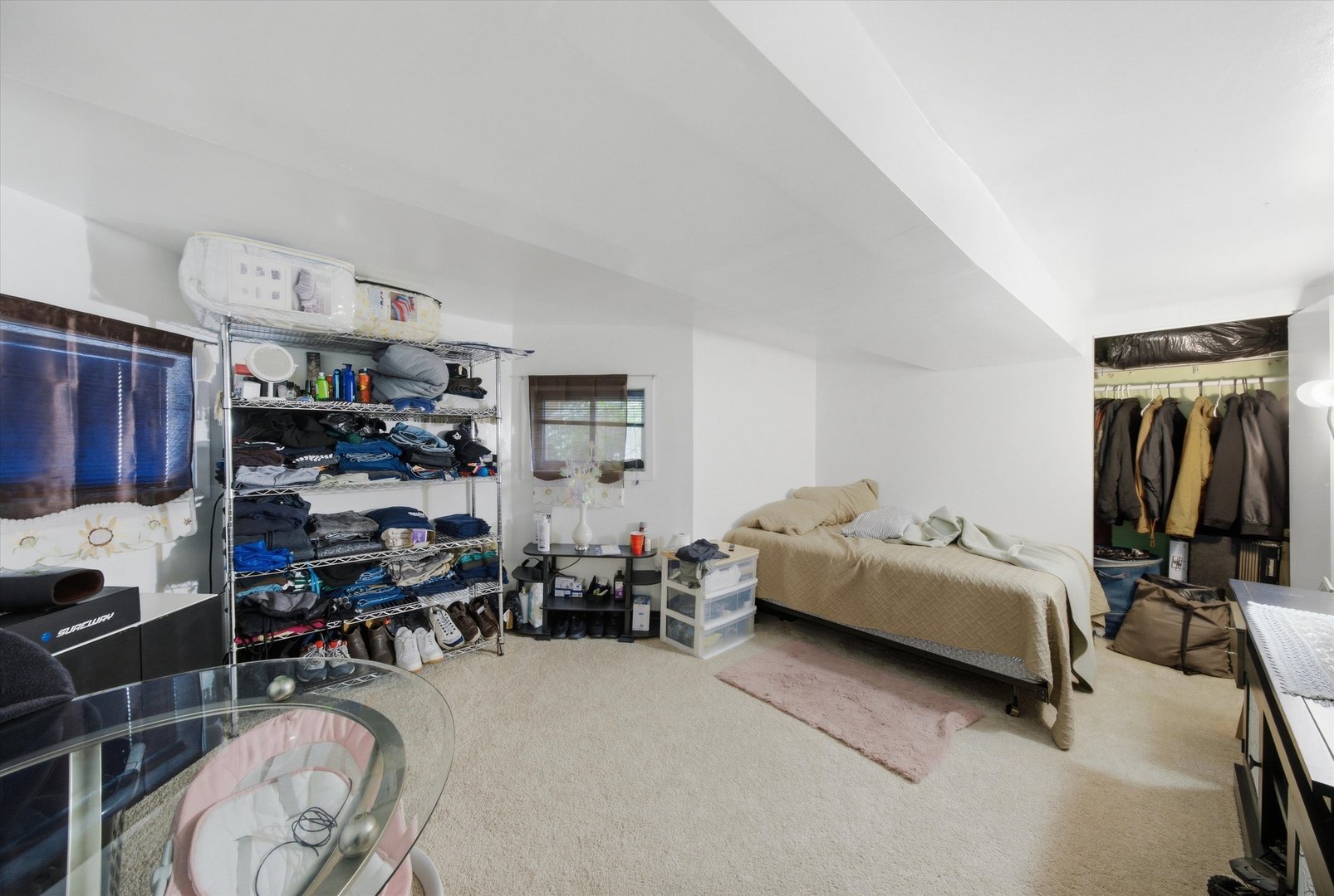 Bedroom with a tan-covered bed, crowded clothing racks, and an open closet.