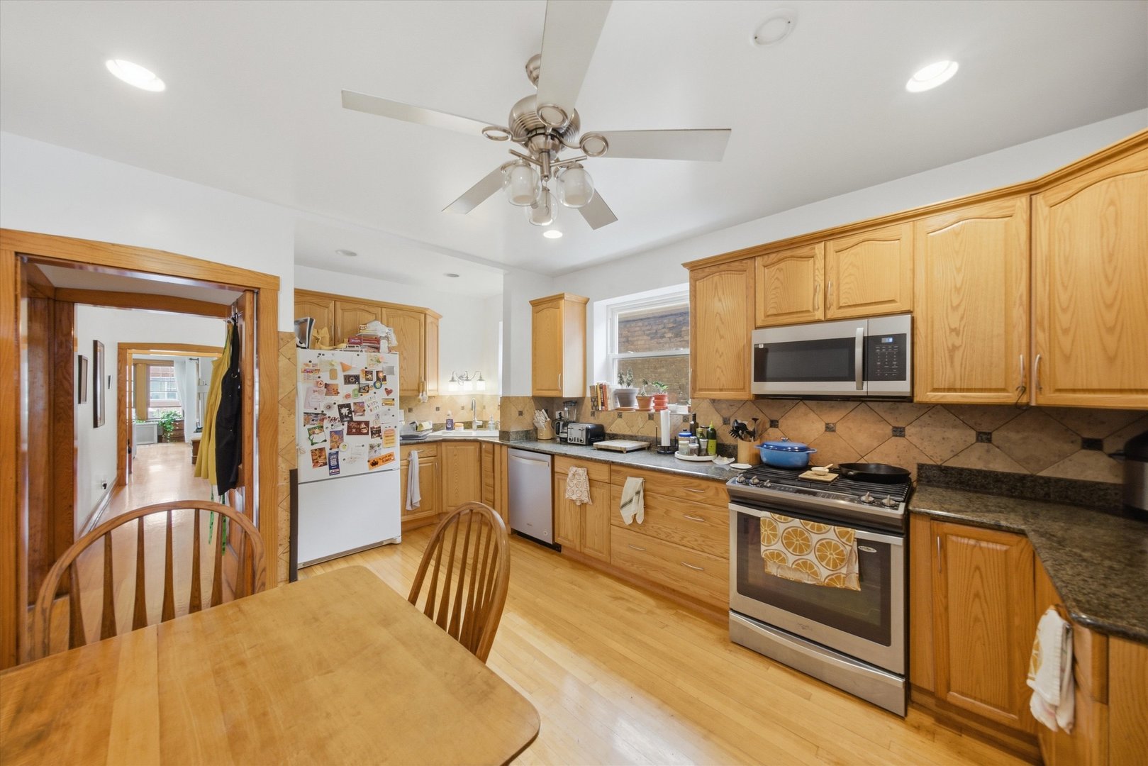 Kitchen with honey-colored wood cabinets, tiled backsplash, stainless steel appliances, and a wooden dining table.