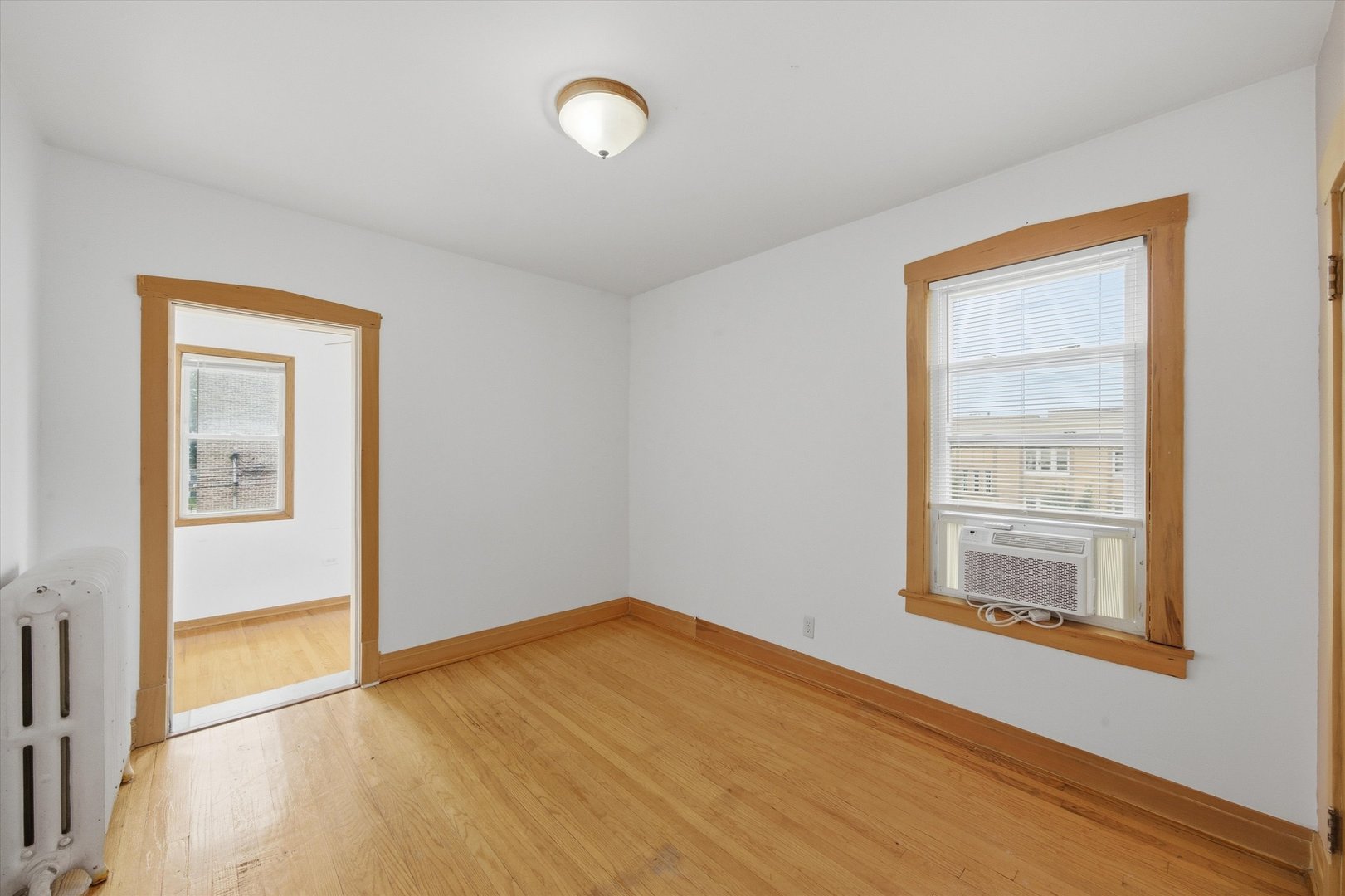 Empty room with hardwood floors, natural wood trim, and a window air conditioner.