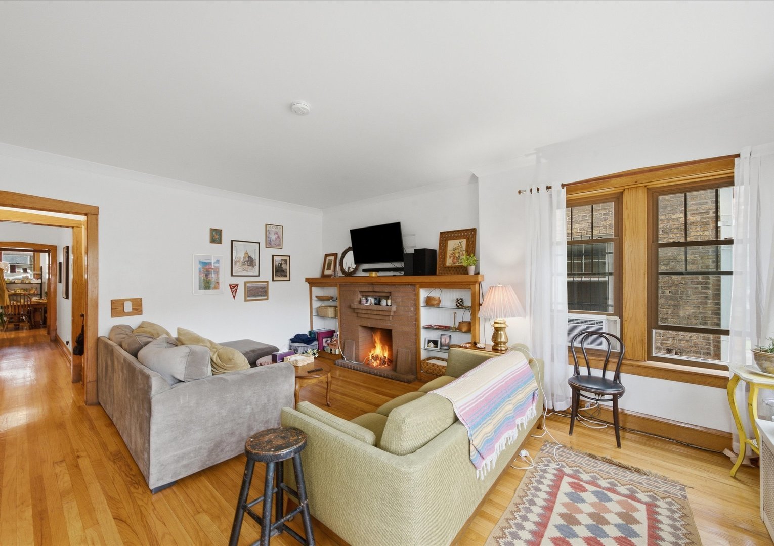 Living room with a brick fireplace, hardwood floors, and large wood-trimmed windows.